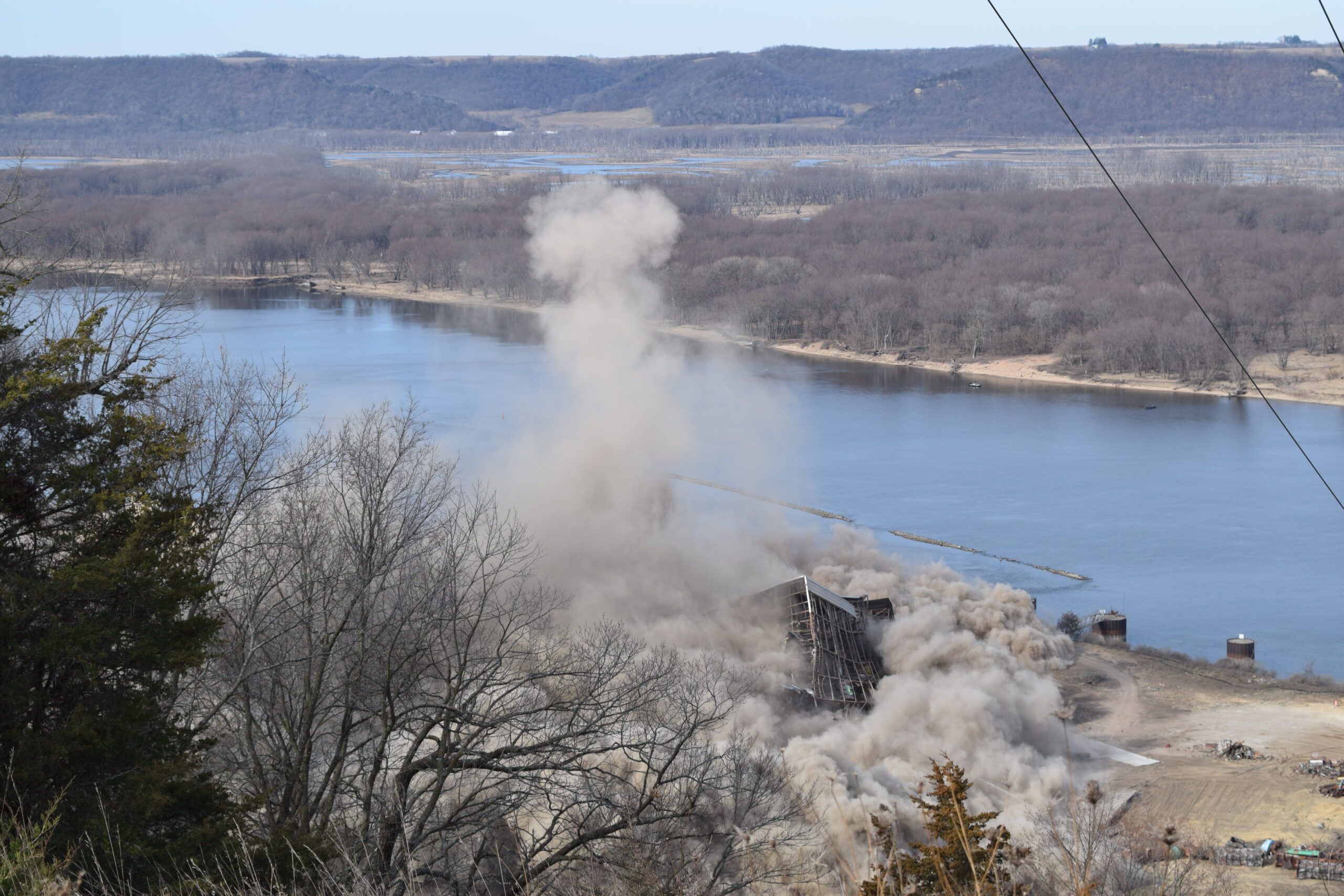 A corner of the steel boiler house peaks through clouds of dust in front of the Mississippi River.