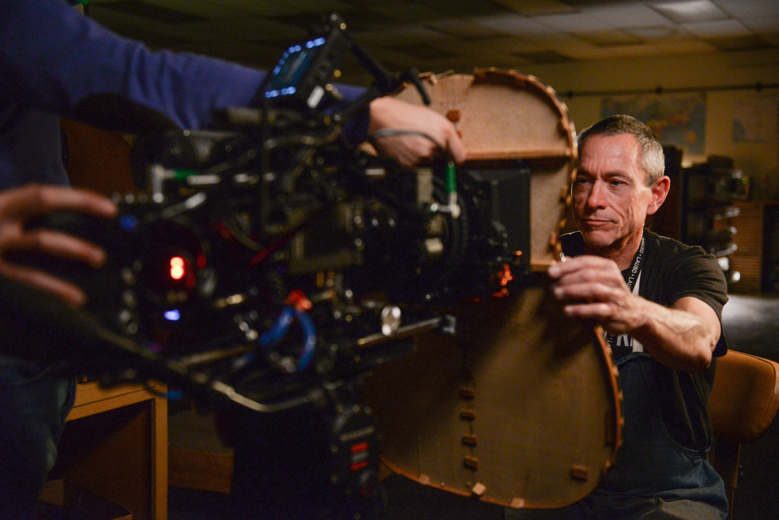 A man sits in front of a camera that is sticking through a hole cut in a guitar. 