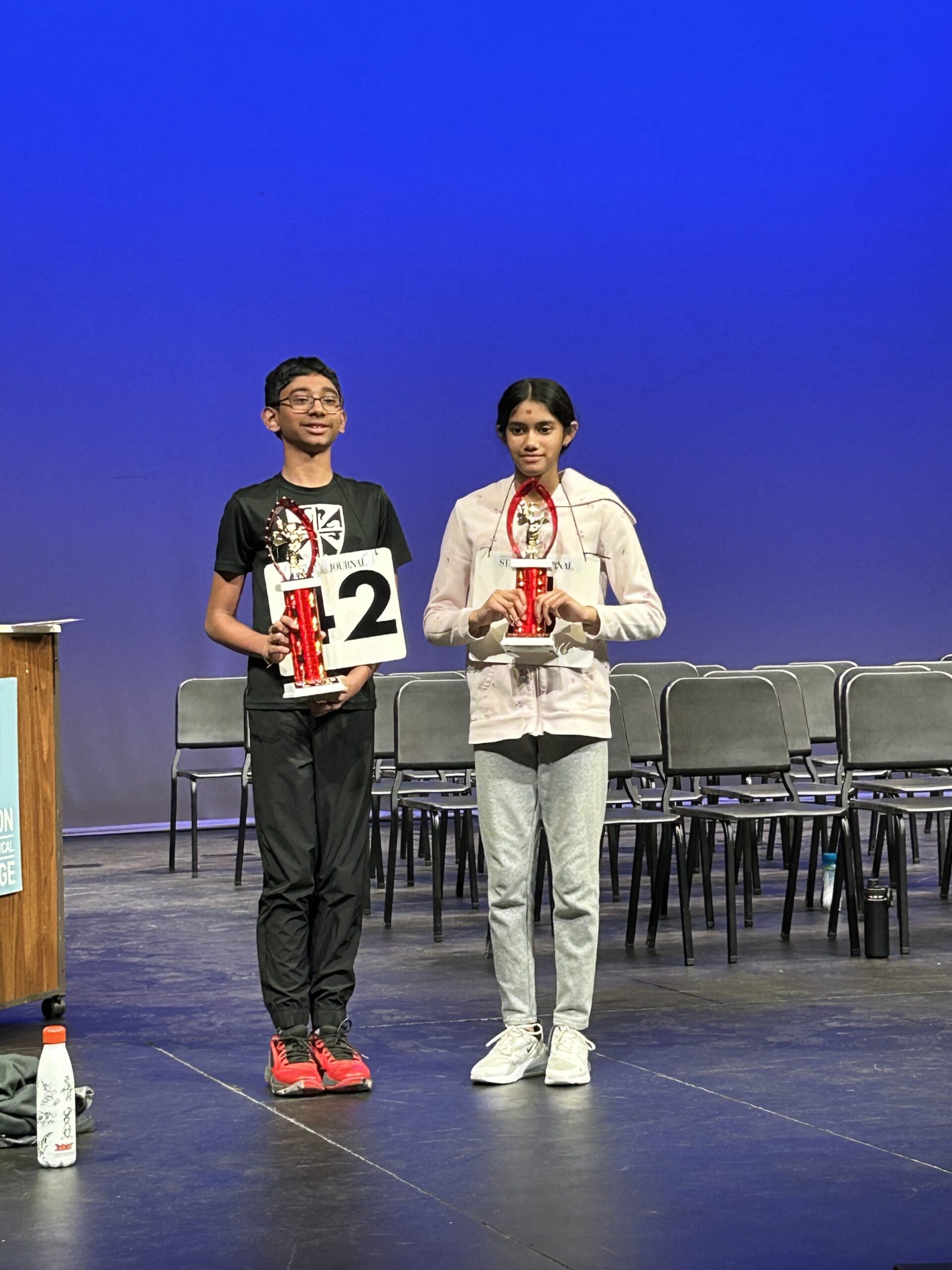The top two-finishers pose on a stage with their trophies after the 2024 Badger State Spelling Bee in Madison