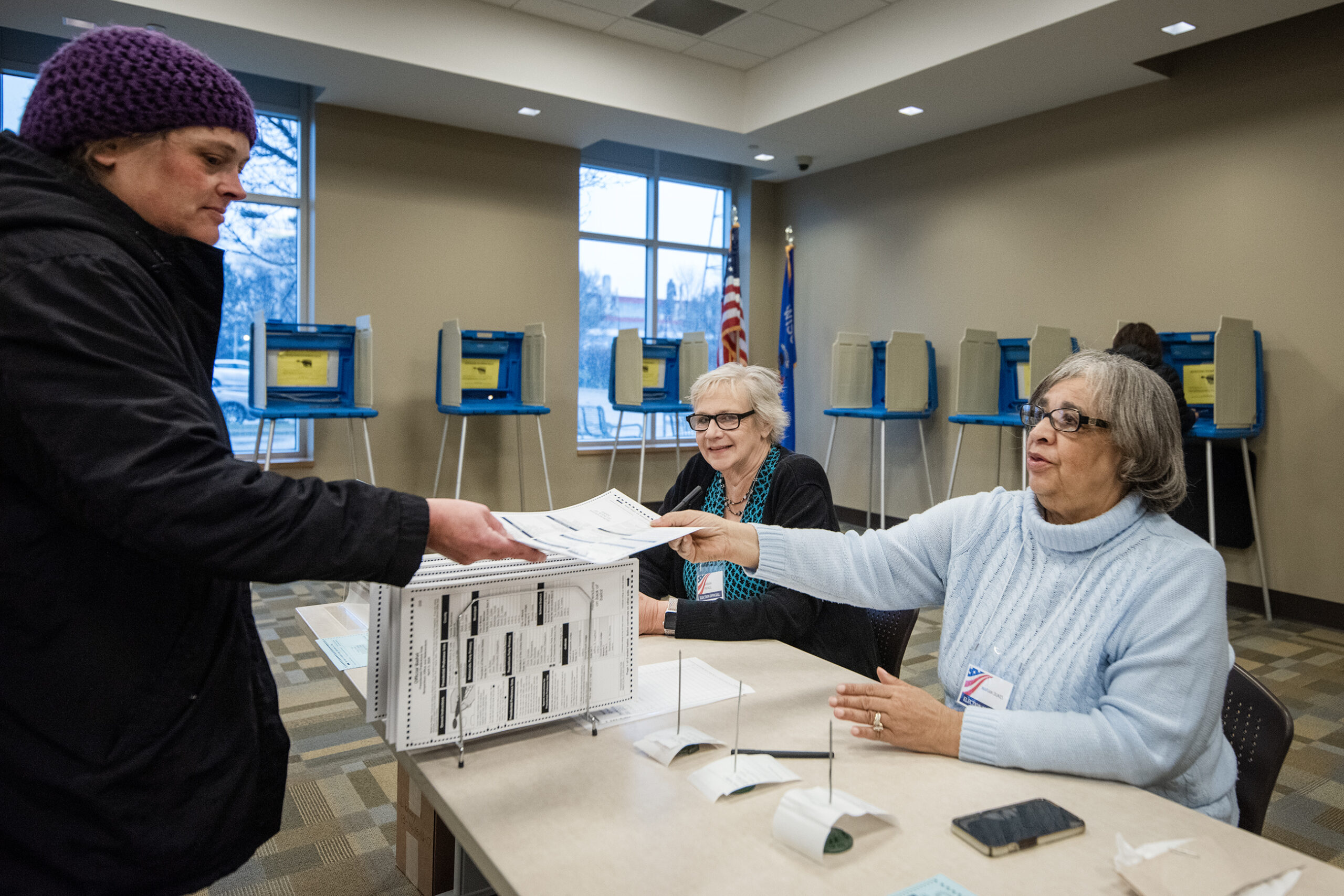 Two ladies sit together at a table. One hands a ballot to a voter.