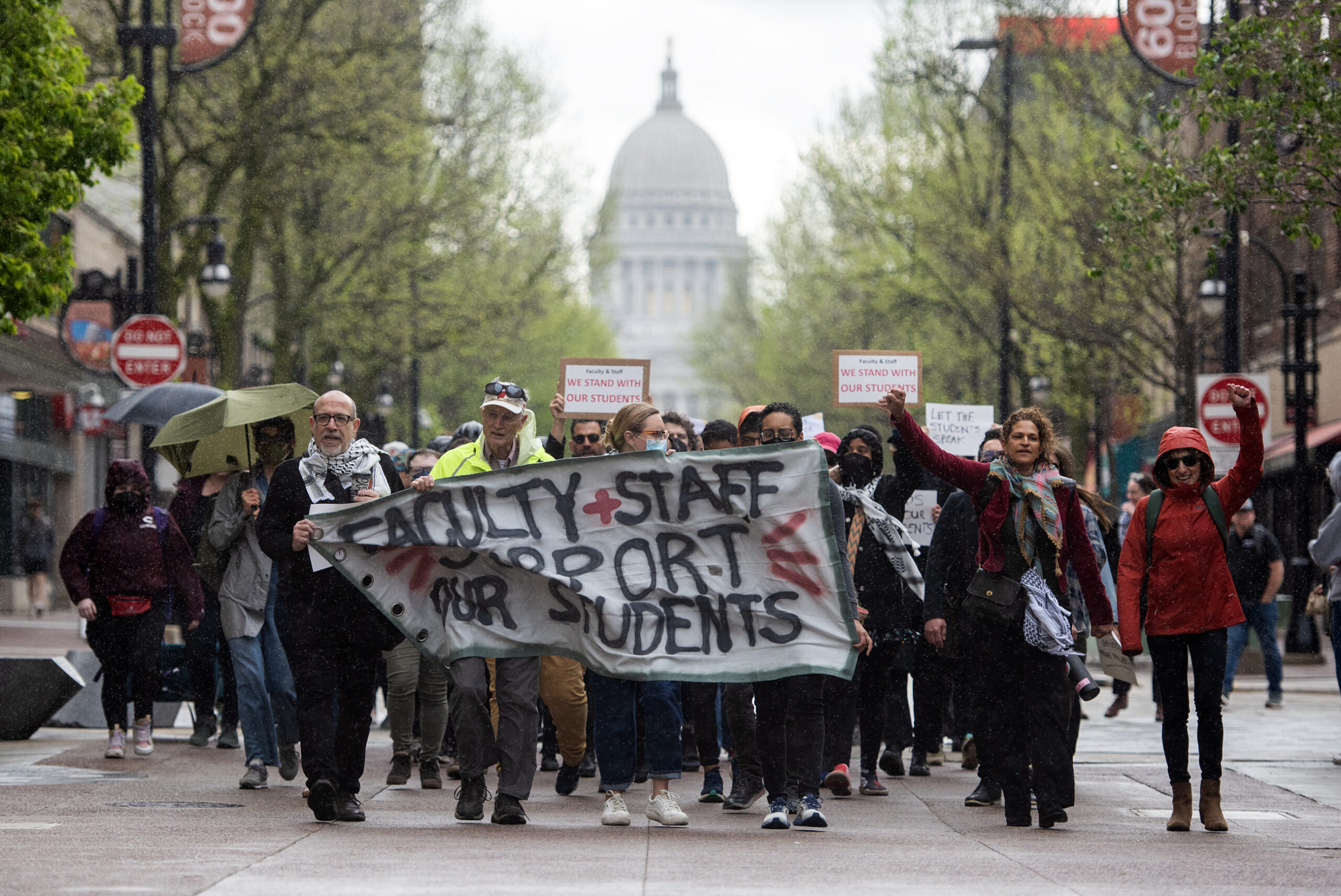 Faculty and staff hold a banner as they walk down State Street. The Wisconsin State Capitol can be seen behind them.