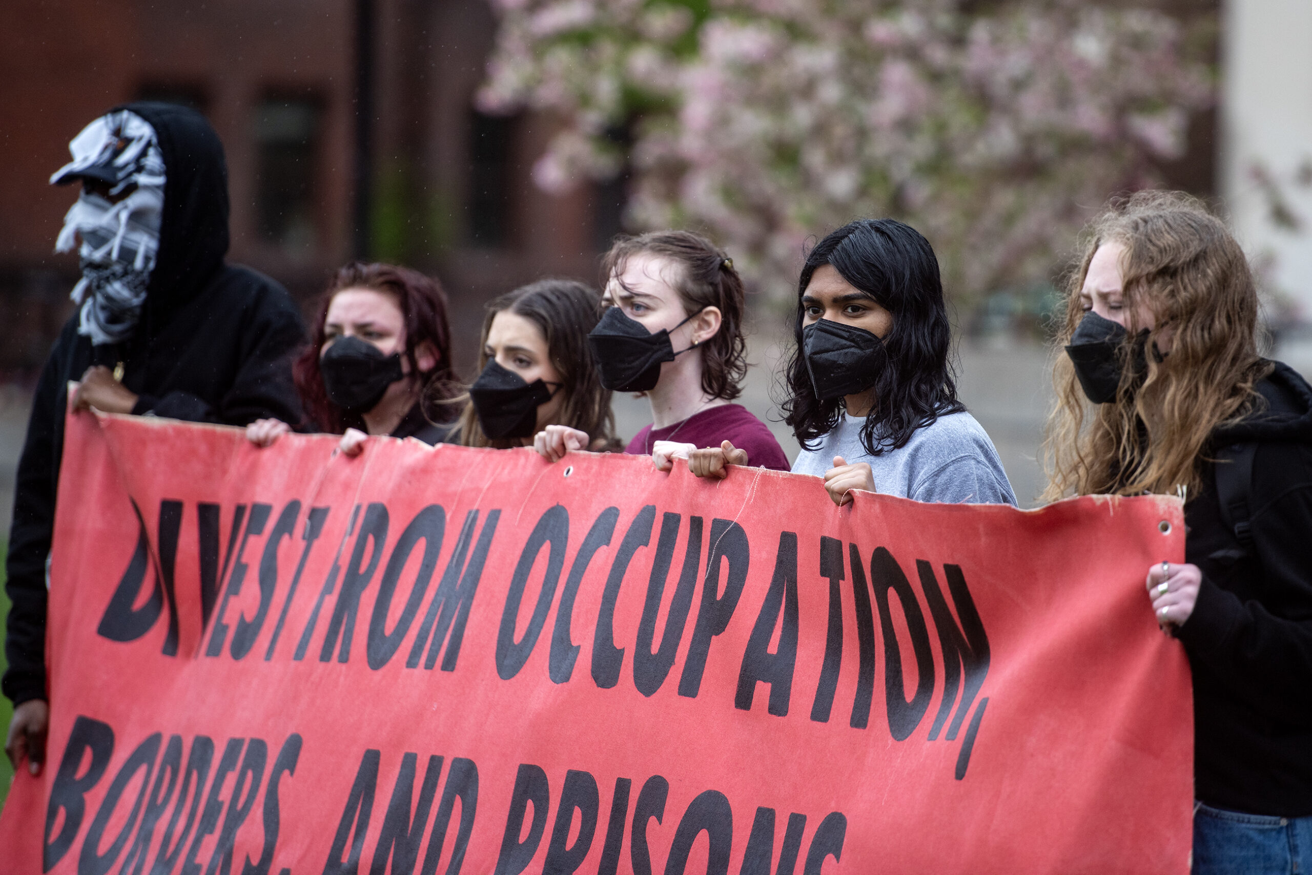 Students hold a red banner that says in part "divest from occupation."