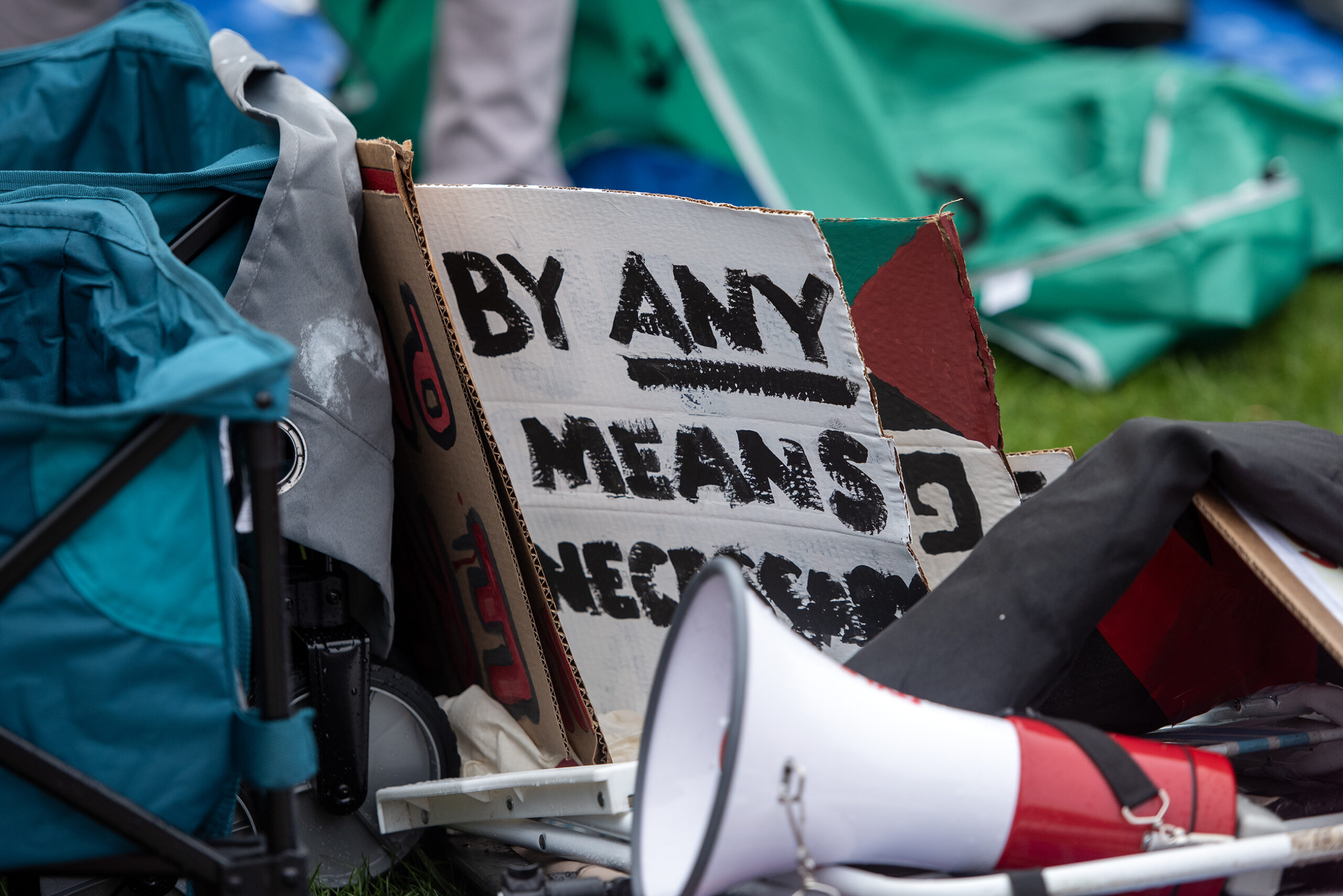 A sign propped up on the ground says "By any means necessary." A megaphone sits nearby as well.