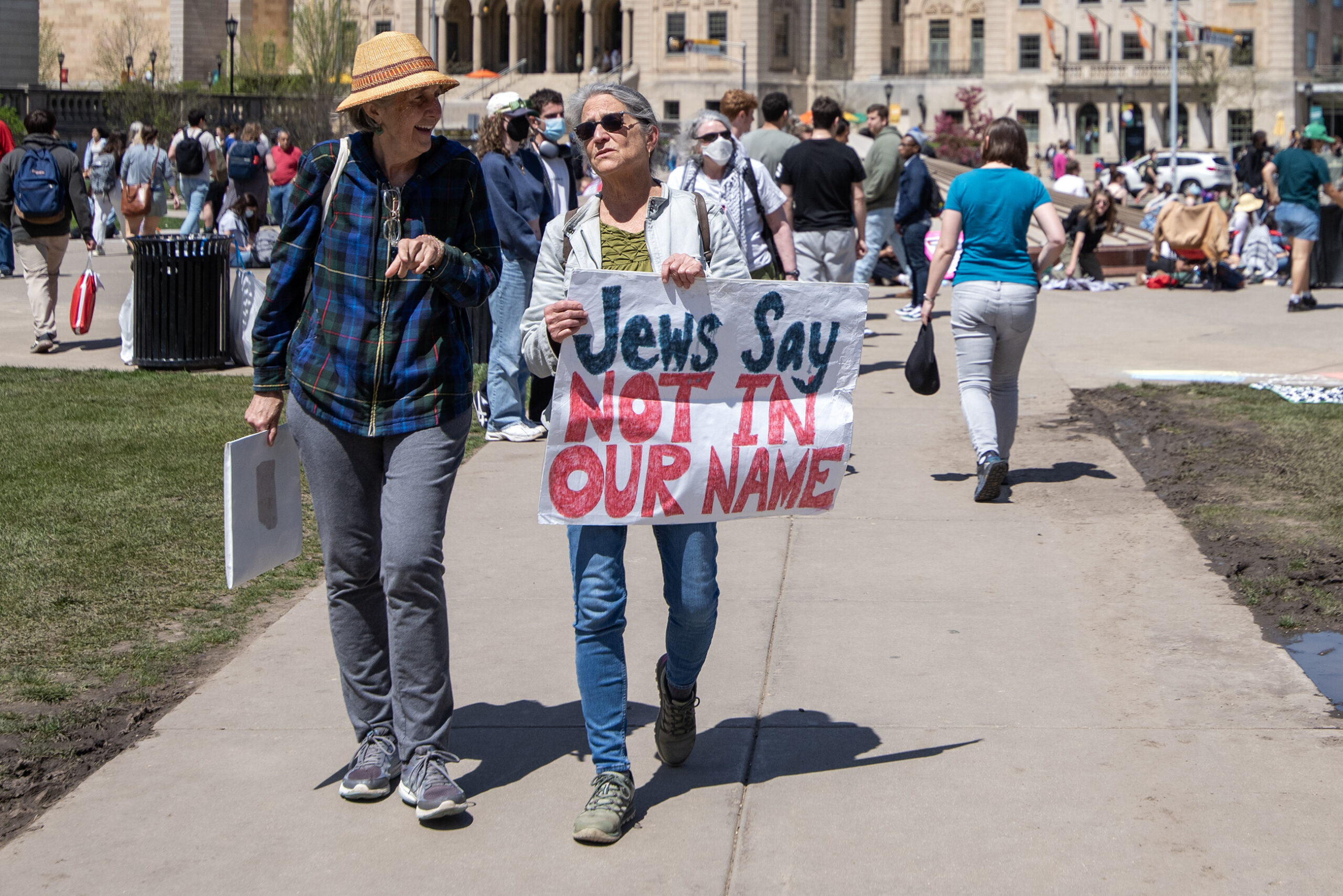 A woman walks with a sign that says "Jews Say Not In Our Name."
