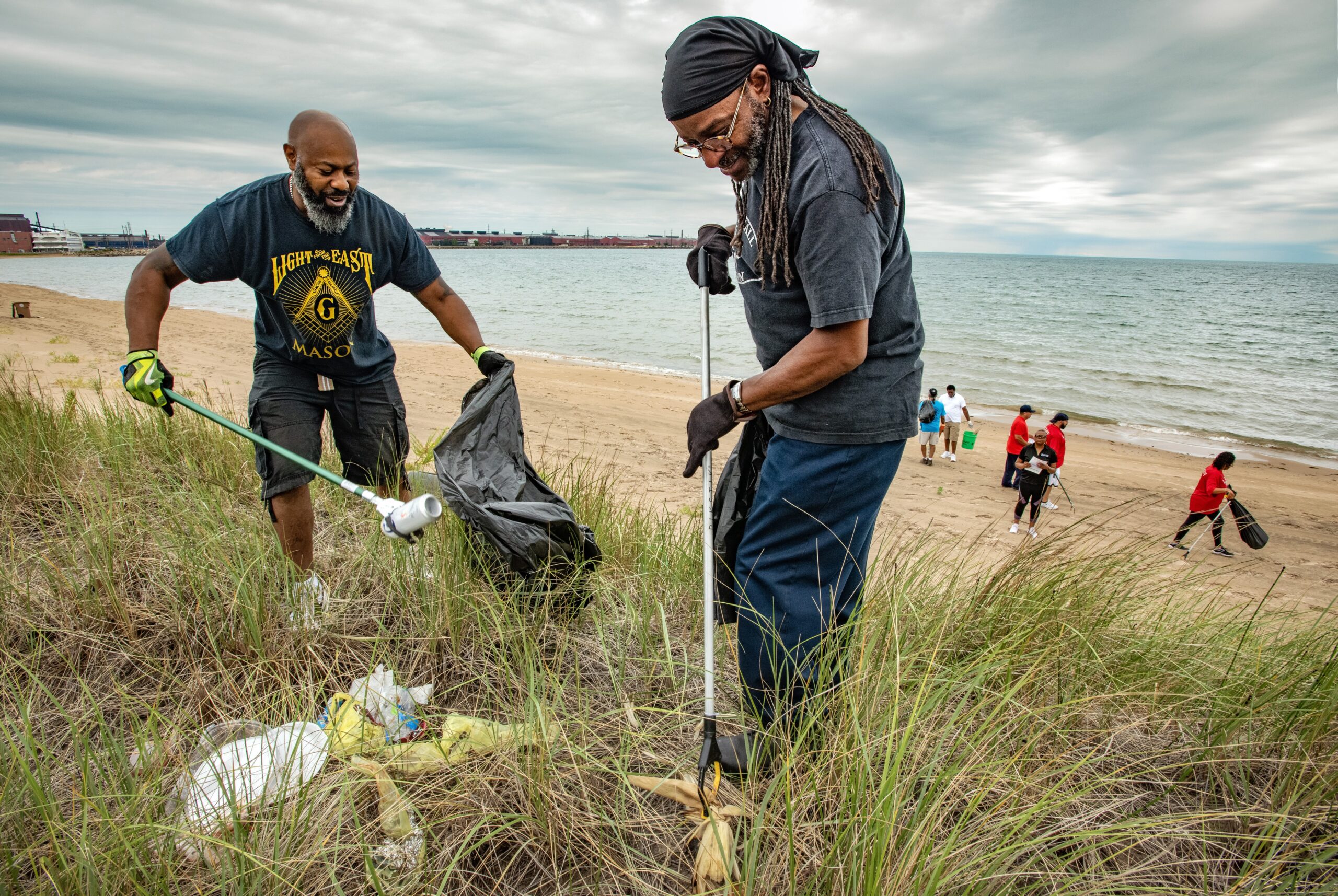 Volunteers put trash into black plastic bags on Great Lakes beach