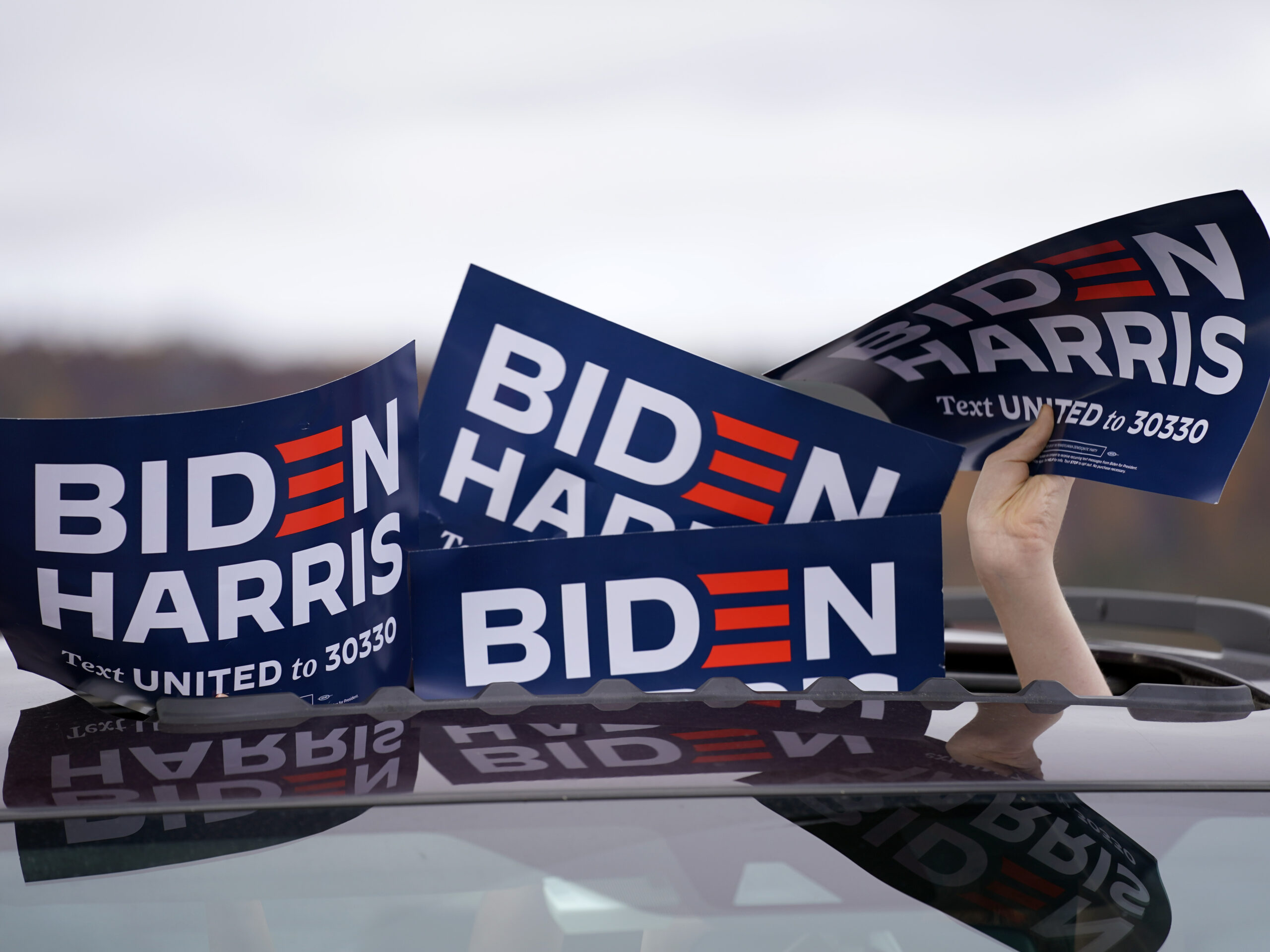 A person holds signs from the sunroof of a vehicle during a campaign event for Joe Biden.