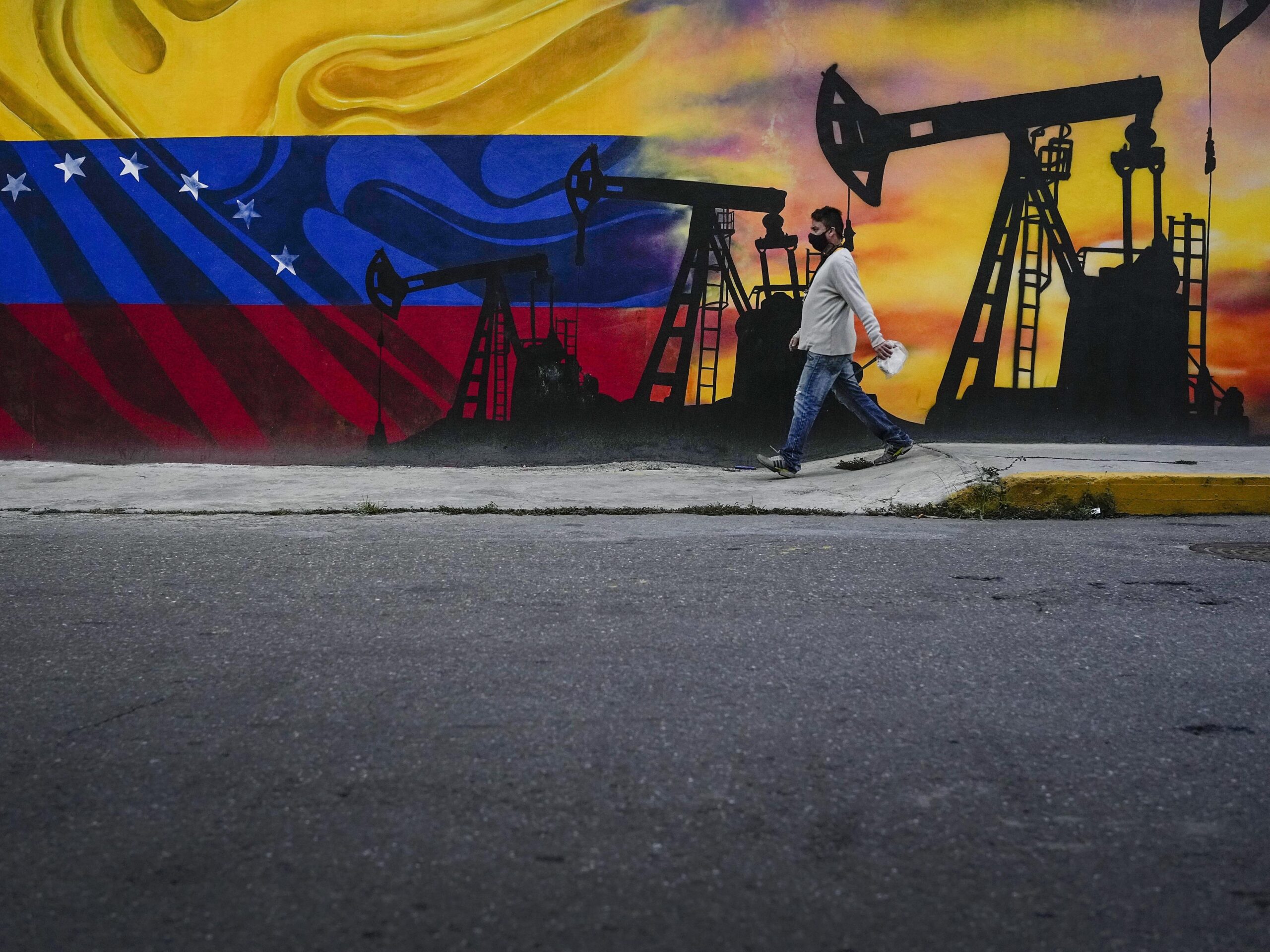 A man walks past a mural featuring oil pumps and wells in Caracas, Venezuela, as the country faces the prospect of the U.S. reimposing oil sanctions.