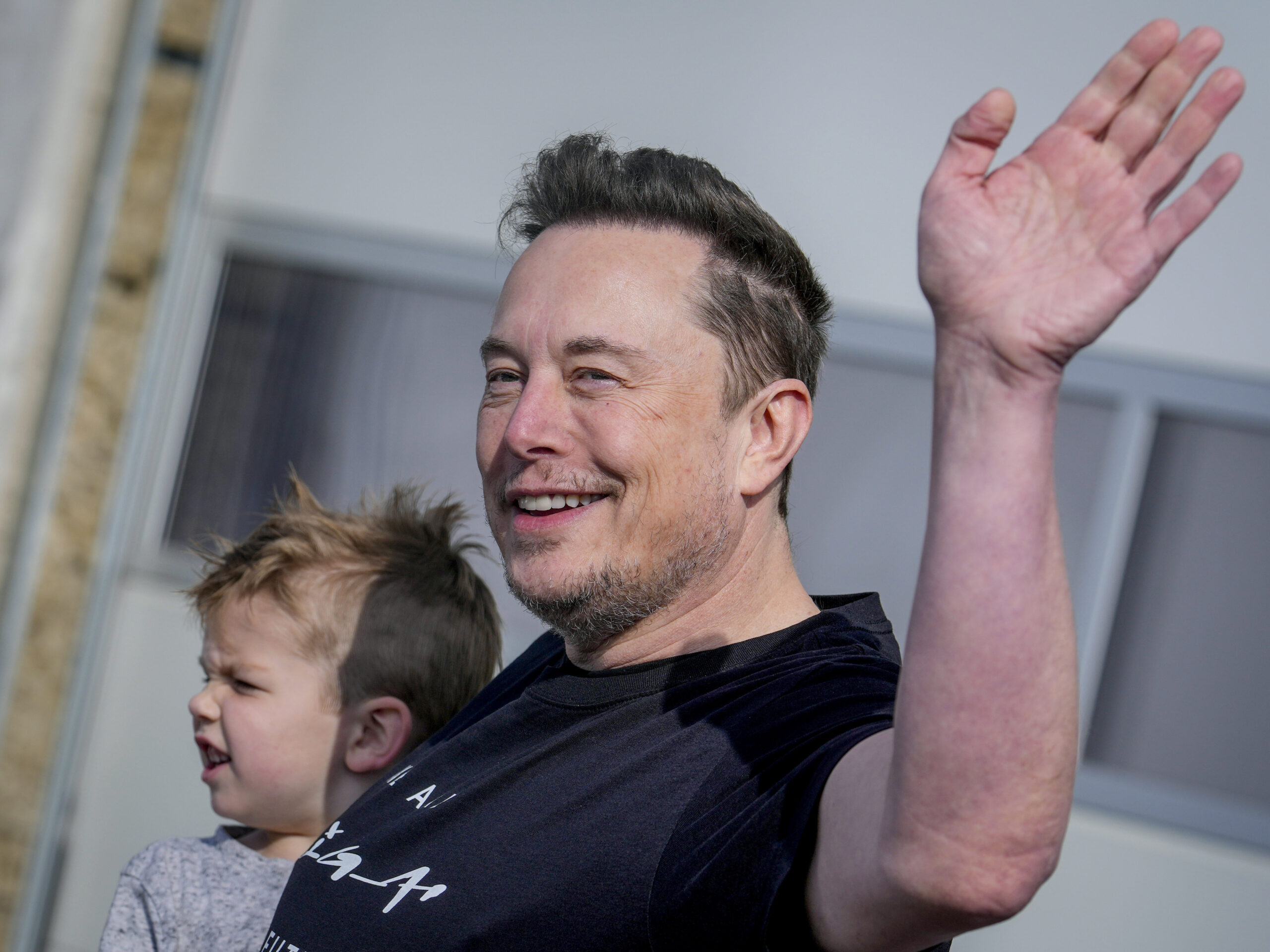 With his son in one arm, Tesla CEO Elon Musk waves while visiting the Tesla Gigafactory in Germany in March.