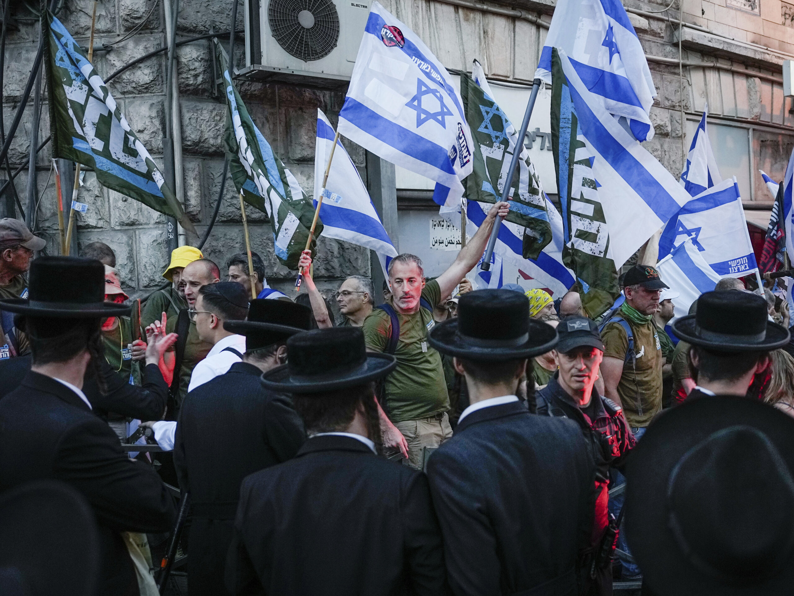 Members of the 'Brothers in Arms' reservist protest group wave Israeli flags during a demonstration in the ultra-Orthodox neighborhood of Mea Shearim, demanding equality in Israel's military service, in Jerusalem on Sunday, March 31, 2024.