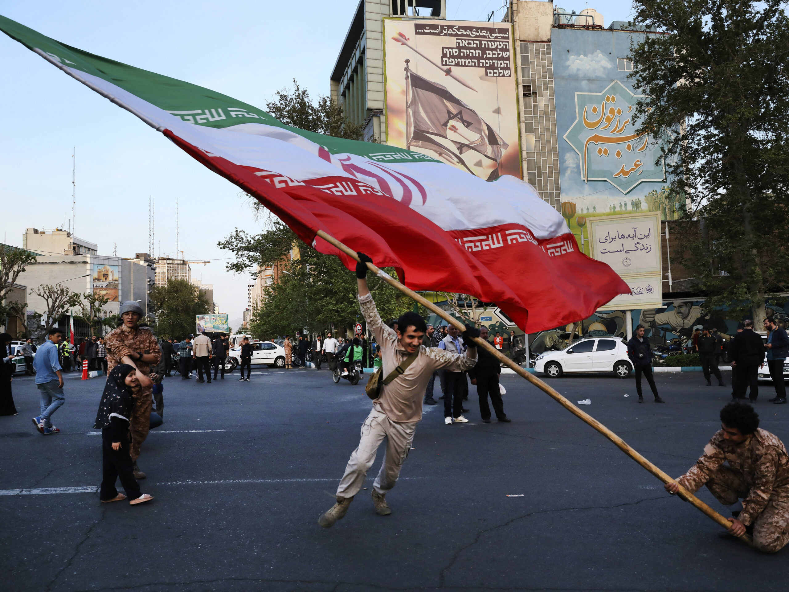 Demonstrators wave a huge Iranian flag in an anti-Israeli gathering in front of an anti-Israeli banner on the wall of a building at the Felestin (Palestine) Sq. in Tehran, Iran, on Monday, April 15, 2024.