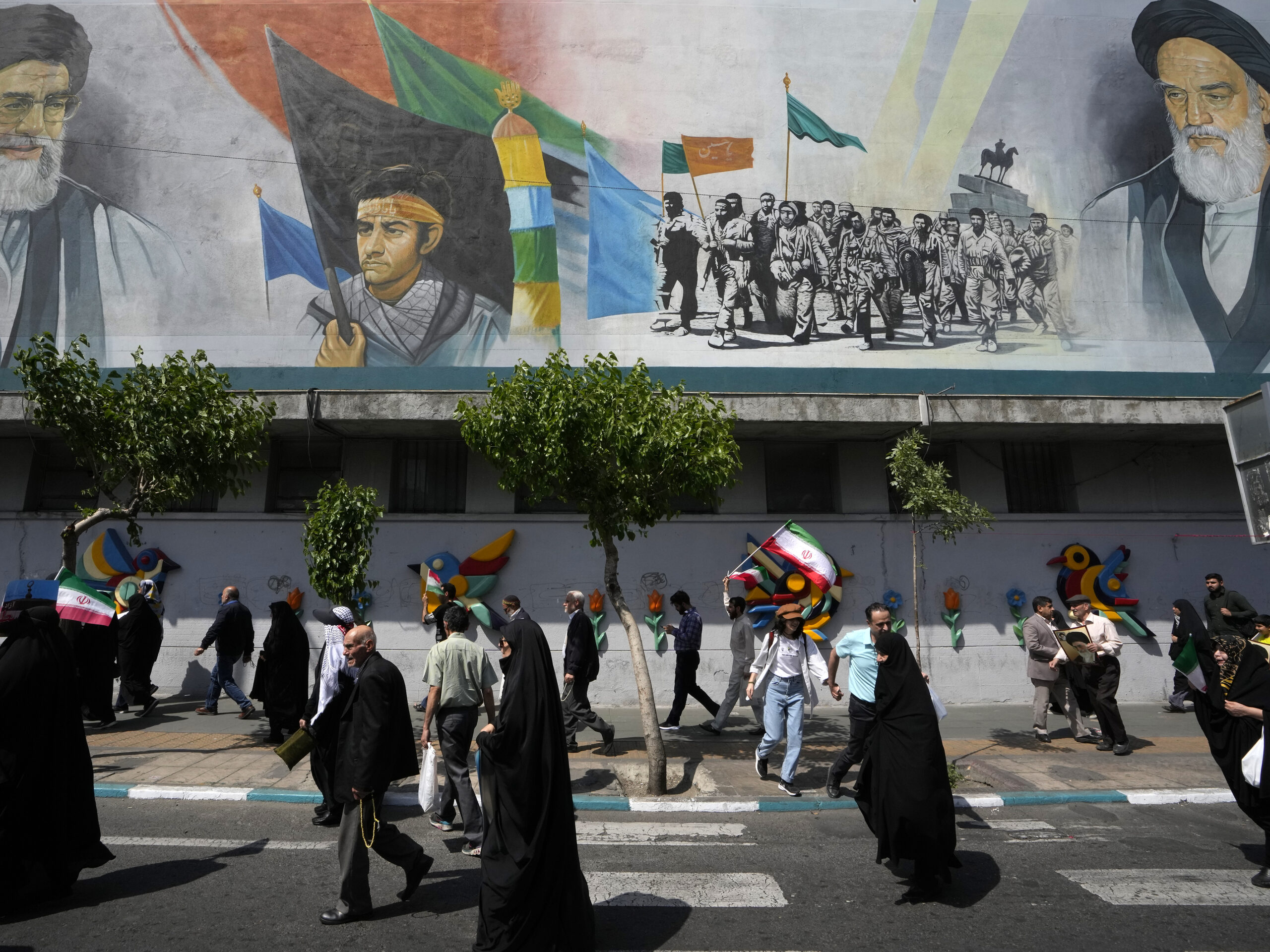 Iranian worshippers walk past a mural showing the late revolutionary founder Ayatollah Khomeini, right, Supreme Leader Ayatollah Ali Khamenei, left, and Basij paramilitary force, in an anti-Israeli gathering after their Friday prayer in Tehran, Iran, on Friday.