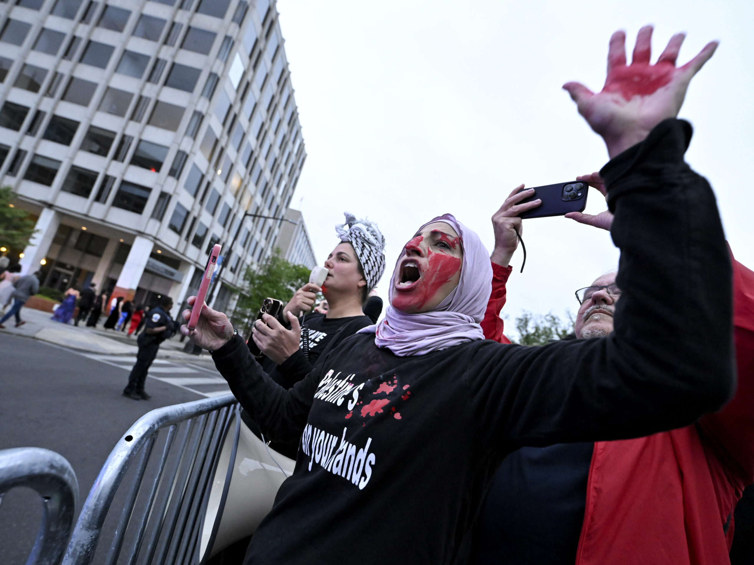 A demonstrator with red paint on their hand and face is seen behind a police barricade during a pro-Palestinian protest over the Israel-Hamas war at the White House Correspondents' Association Dinner, Saturday April 27, 2024, in Washington.
