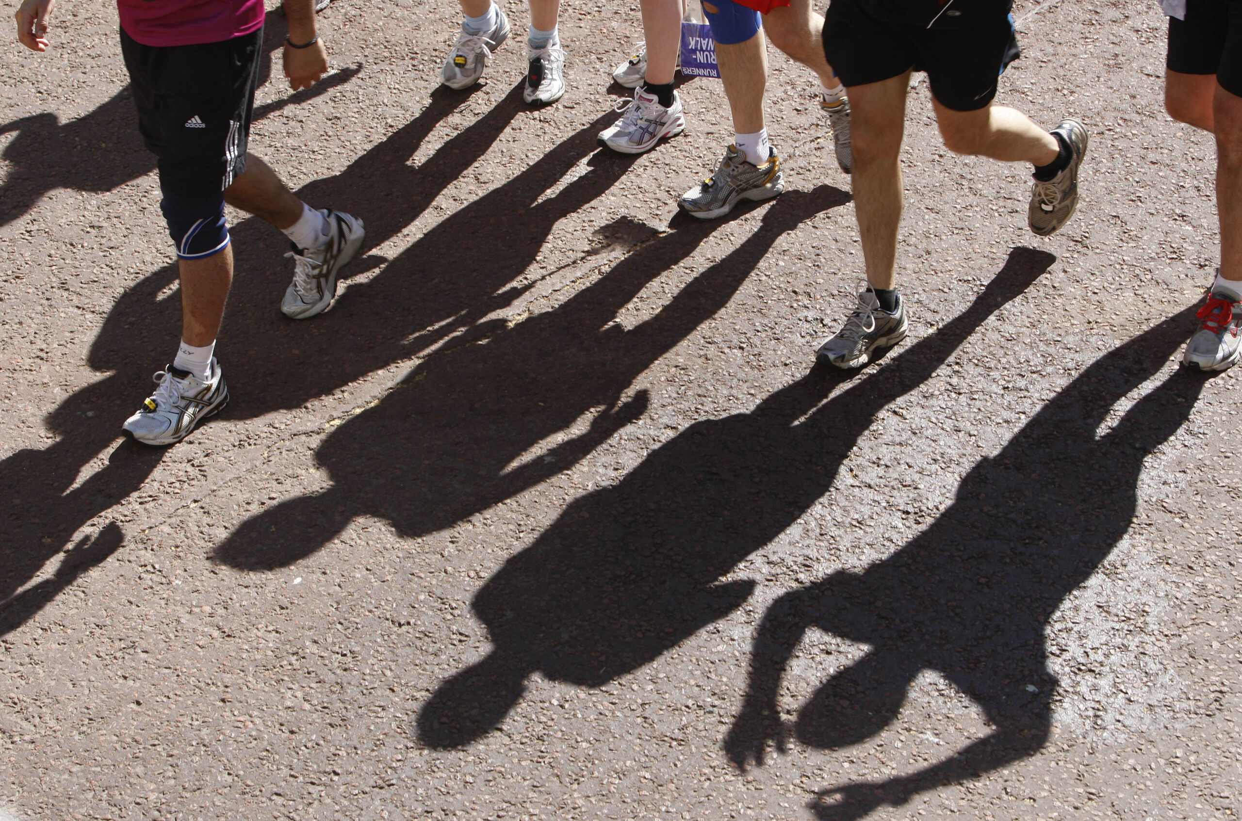 Only the legs of a few runners are seen striking the pavement. Their shadows are also on the pavement.