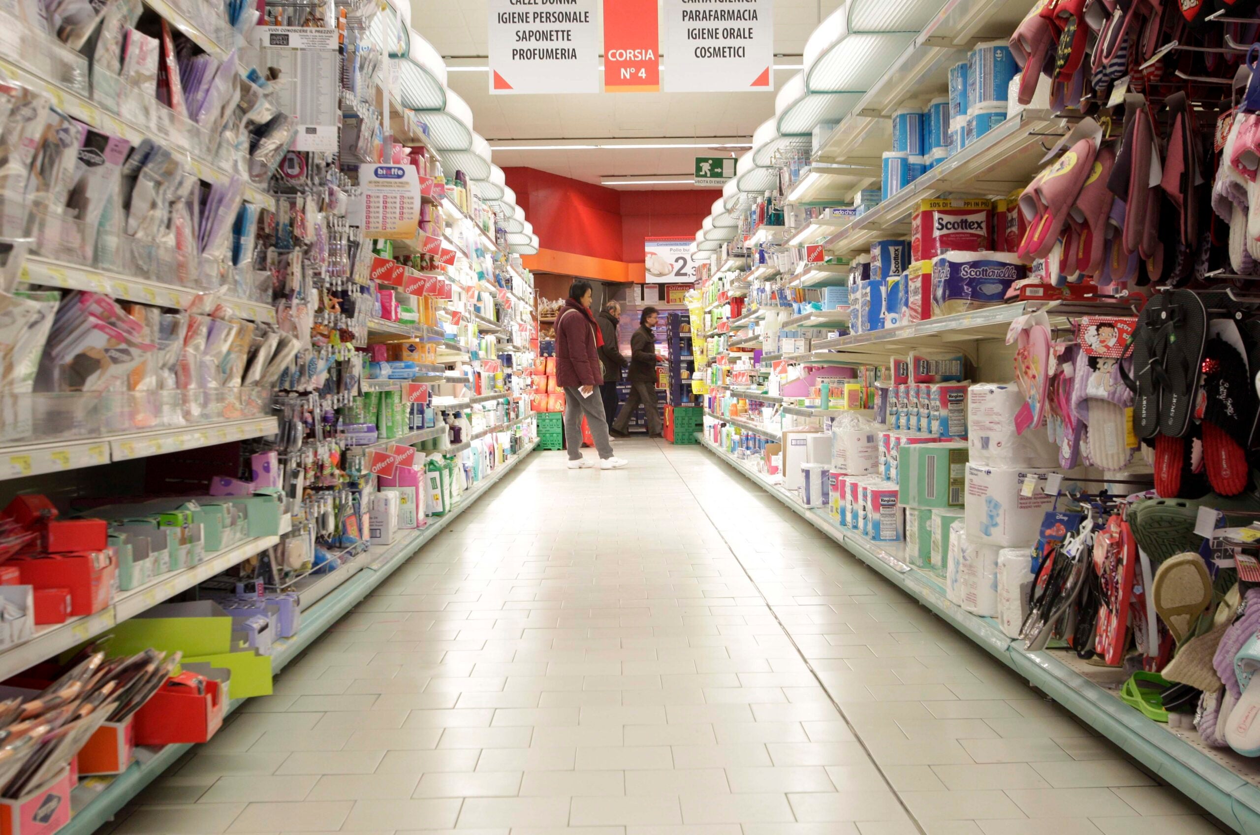 Looking down an isle of a grocery store with sandals, toilet paper and hygience products.