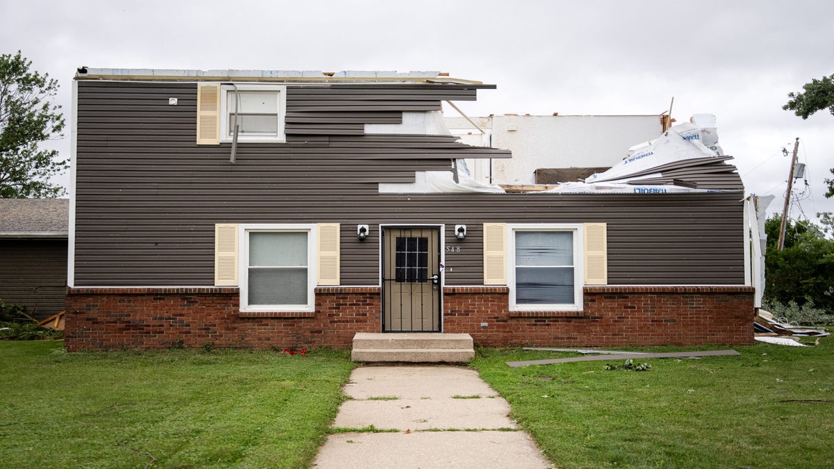 A house with the roof ripped off and the front siding severely damaged.