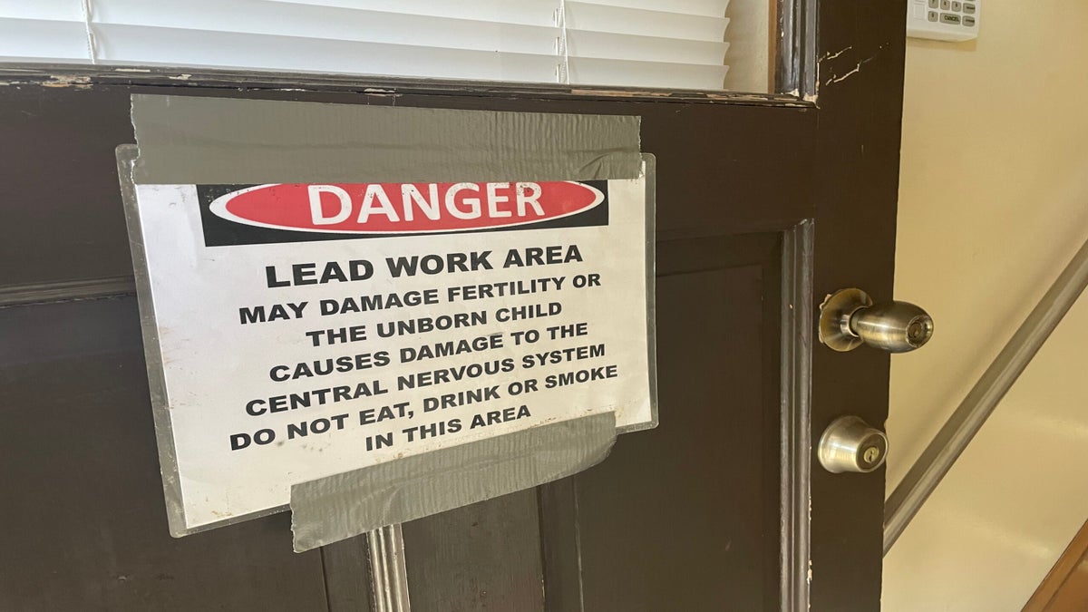 A door with a sign that reads: Danger. Lead work area may damage fertility or the unborn child, causes damage to the central nervous system. Do not eat, drink or smoke in this area.