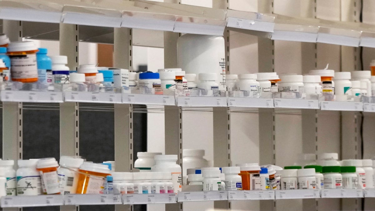 Shelves filled with various prescription medication bottles, organized in rows at a pharmacy or medical facility.