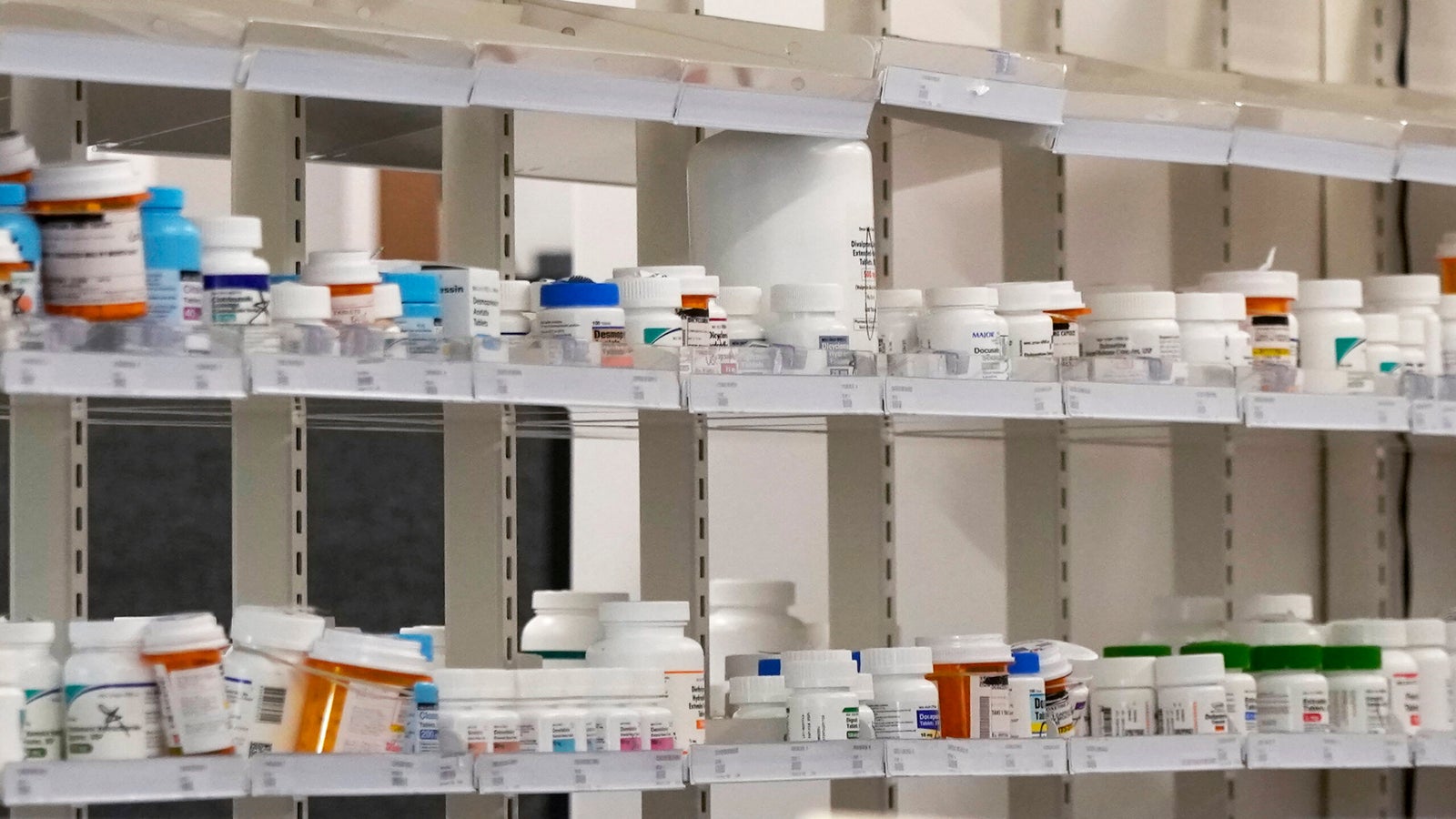 Shelves filled with various prescription medication bottles, organized in rows at a pharmacy or medical facility.
