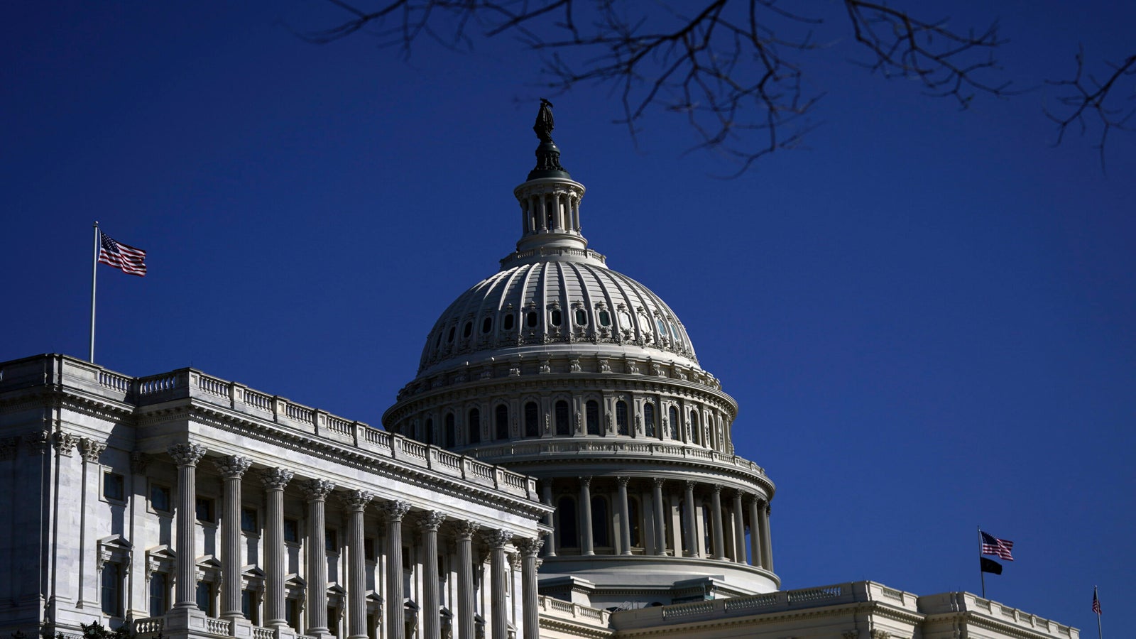 The U.S. Capitol building dome against a clear blue sky, with two American flags visible.