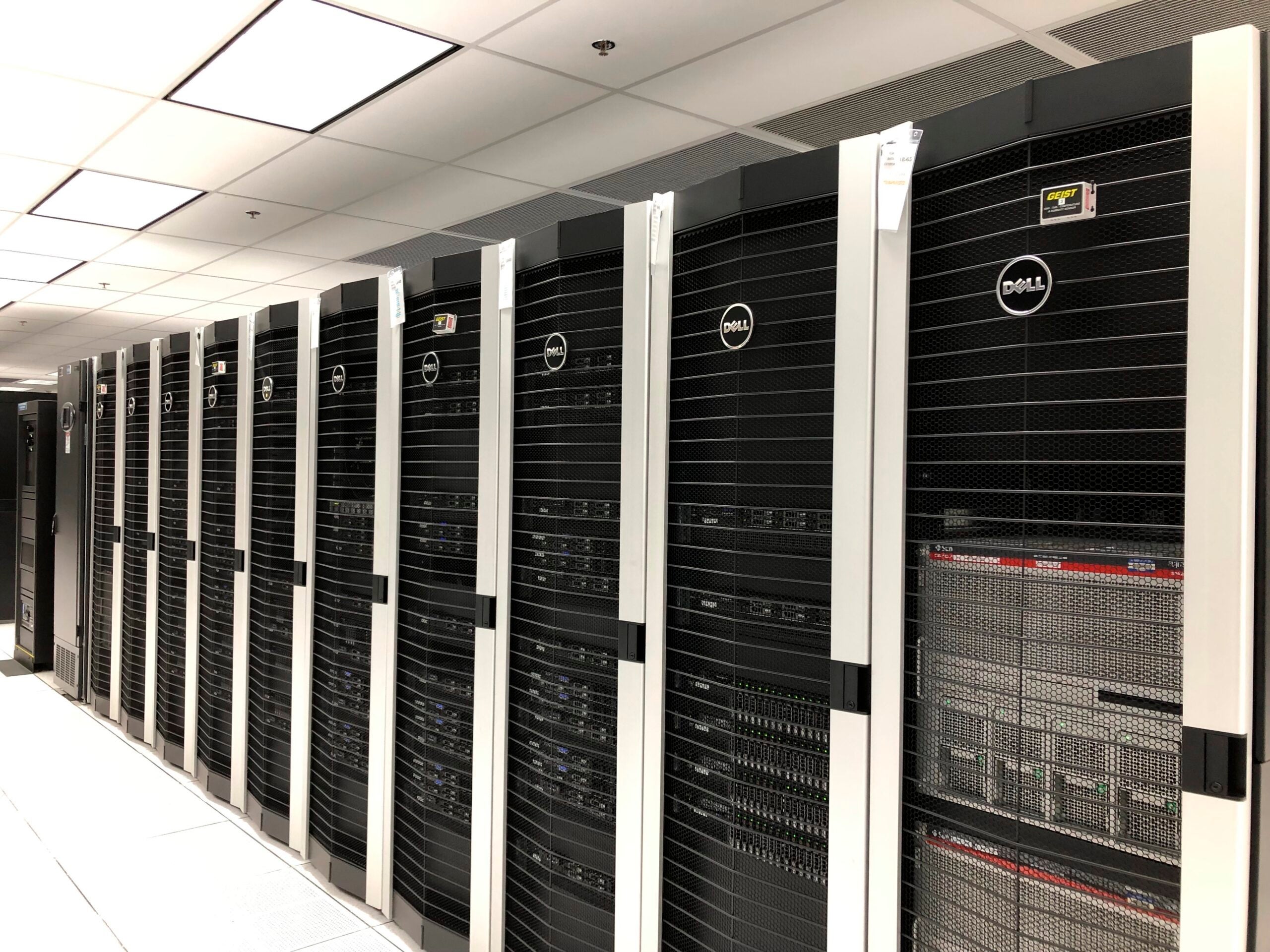 A row of black Dell server racks in a brightly lit data center with white tiled floors and ceiling panels.