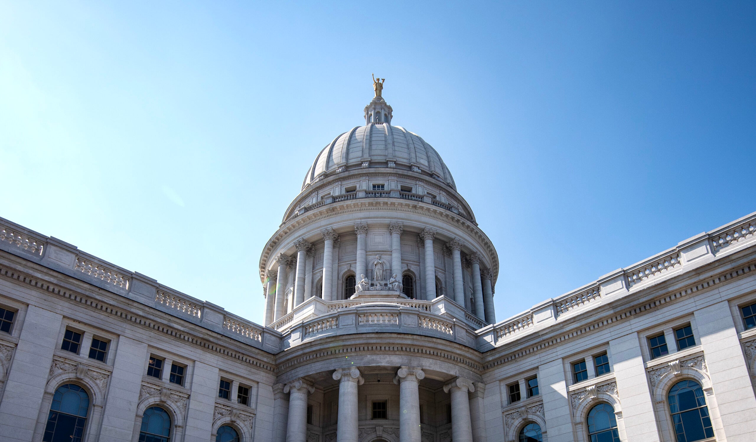 White stone government building with a large central dome and blue sky in the background.