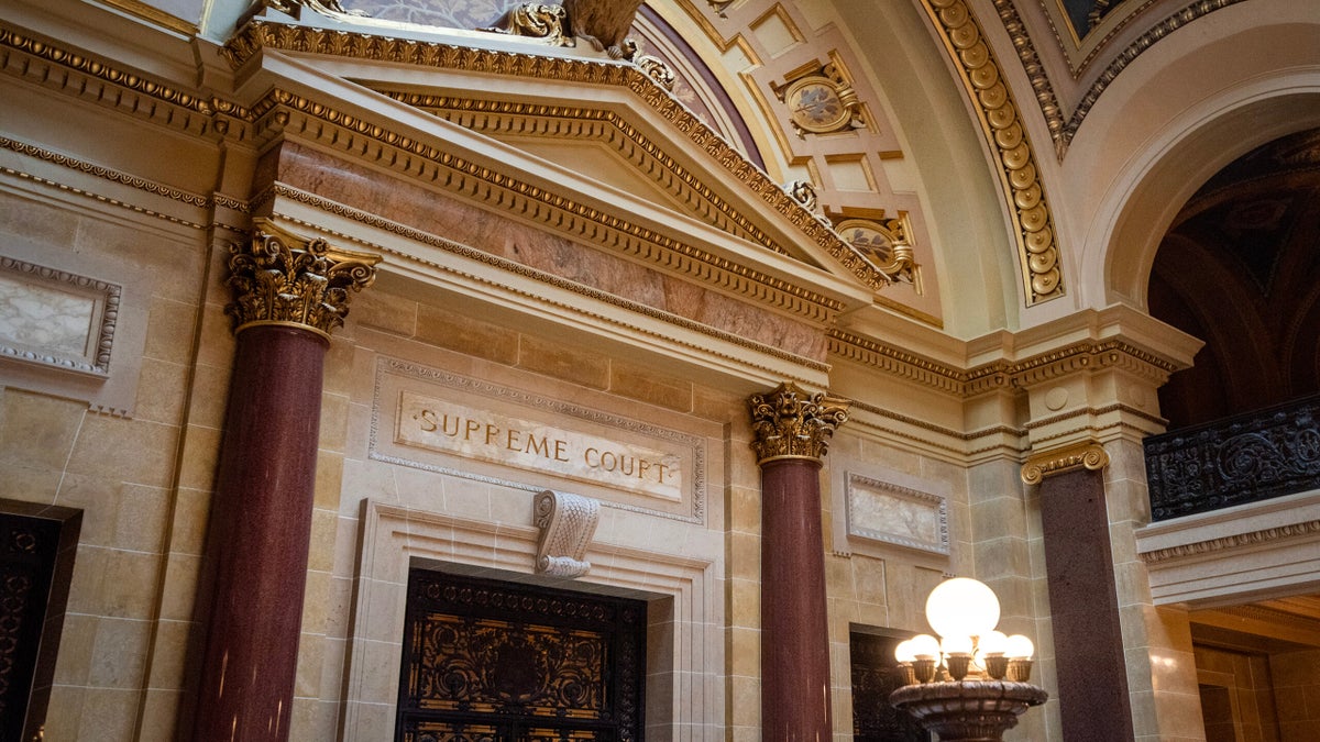 Ornate interior of a government building featuring a sign that reads SUPREME COURT, marble columns, and decorative molding.