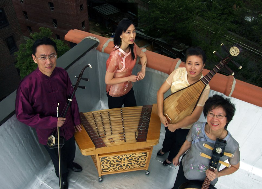 Four people stand on a rooftop with traditional Chinese musical instruments, including a yangqin, erhu, pipa, and ruan.