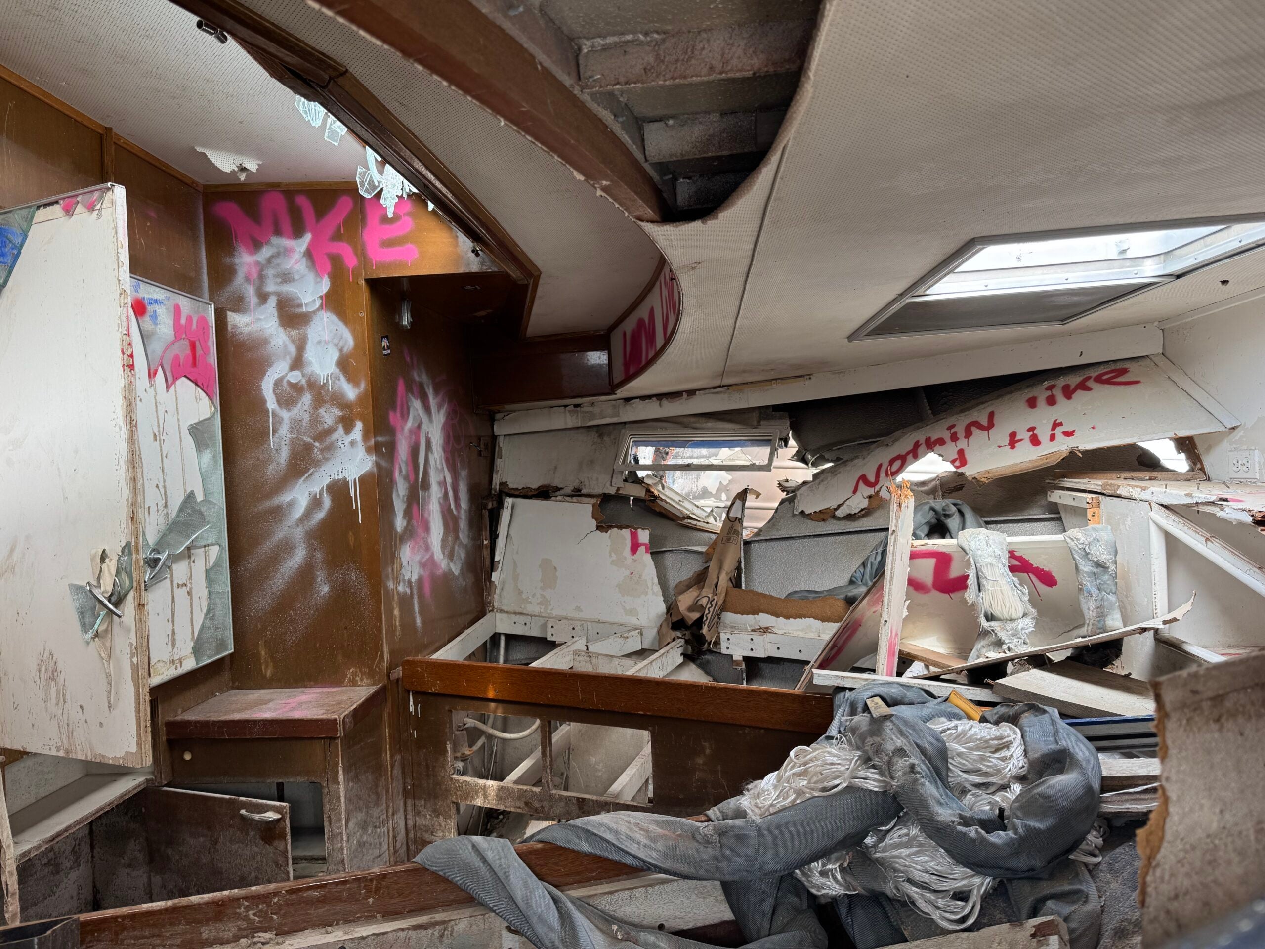The interior of a heavily damaged boat with broken wood, debris, and graffiti reading NIKE and Nothin like it sprayed on the walls.