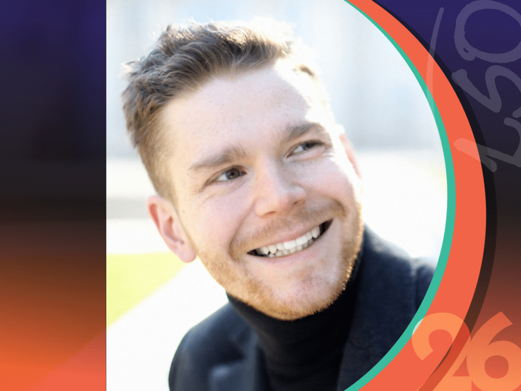 A man with short light brown hair and a trimmed beard, wearing a black turtleneck, smiles and looks to his left. There are colorful graphic elements along the image edges.