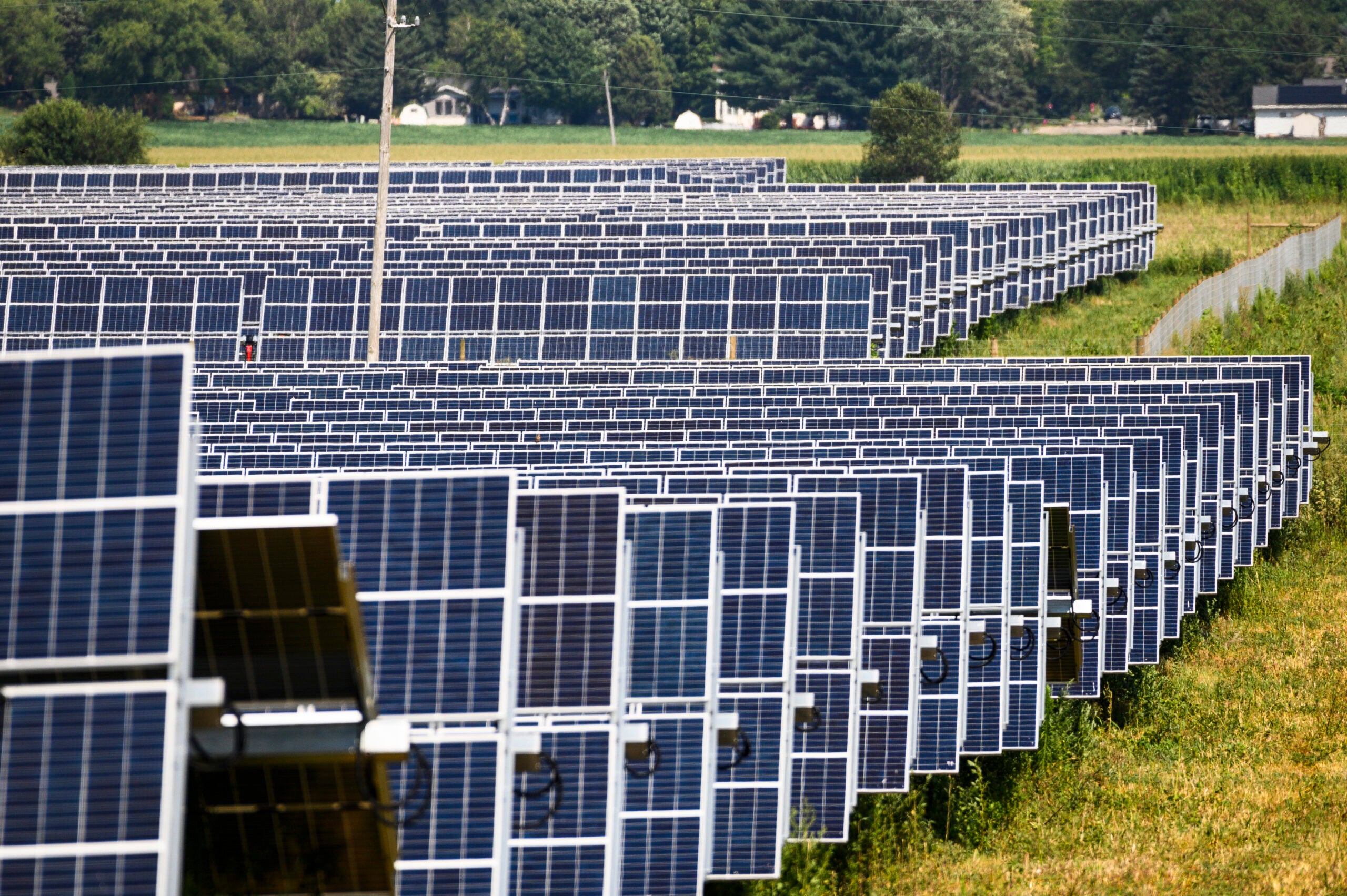 Rows of solar panels are installed in a large field, generating renewable energy under a partly cloudy sky.