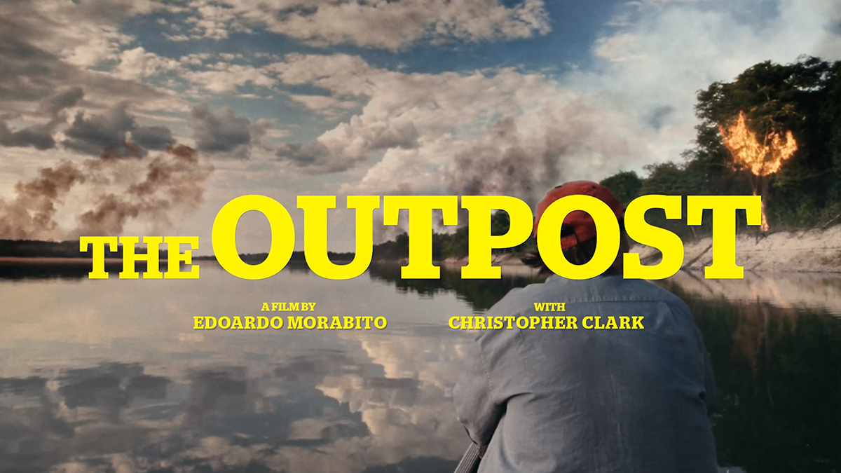 A person in a boat on a calm river with smoke rising in the background; large yellow text reads The Outpost, a film by Edoardo Morabito with Christopher Clark.