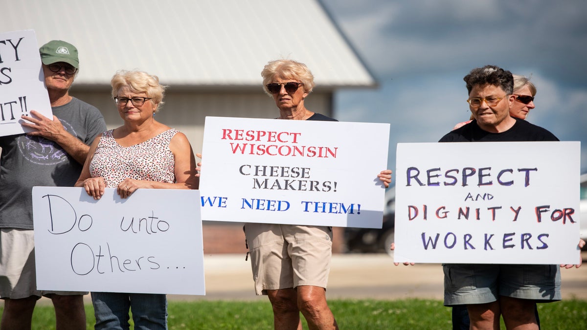 A group of people stand outside holding signs that support cheese makers and call for respect, dignity, and kindness for workers and others.