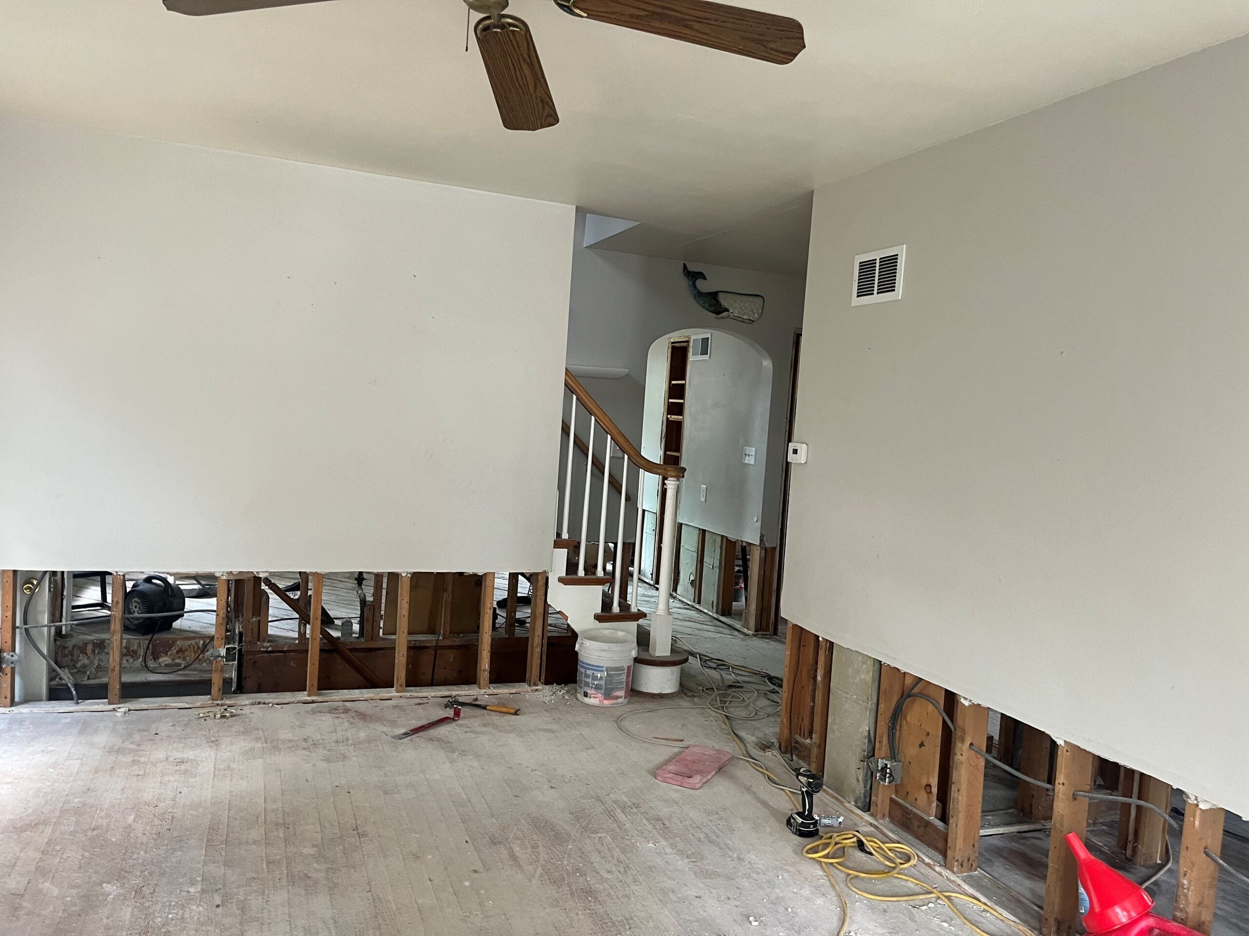 A partially renovated room with exposed lower wall studs, construction materials on the floor, and visible stairs in the background.