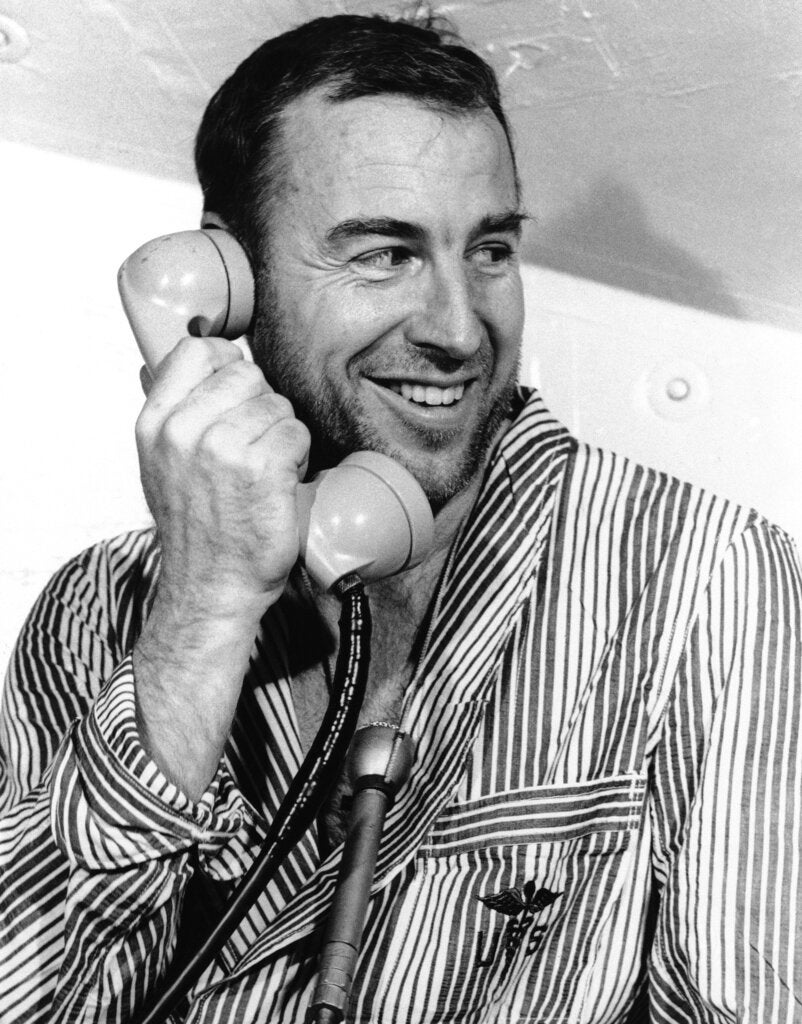 A man wearing striped clothing is smiling while holding a vintage telephone receiver to his ear.