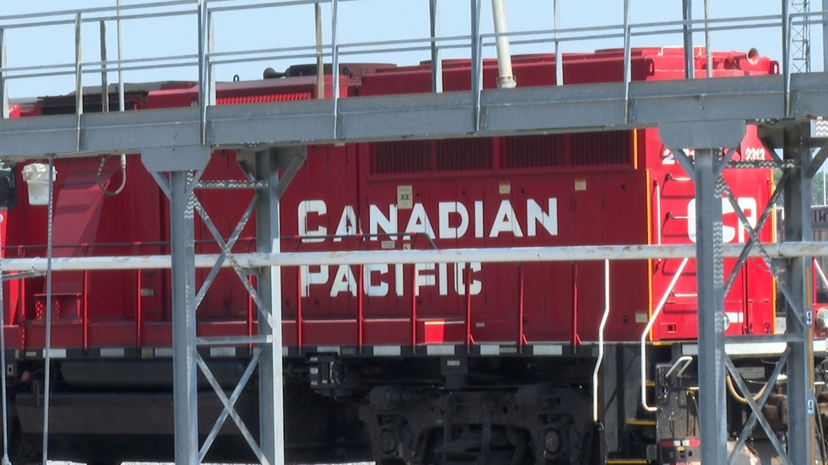 A red Canadian Pacific locomotive is partially obscured by metal railings and structures in an industrial setting.