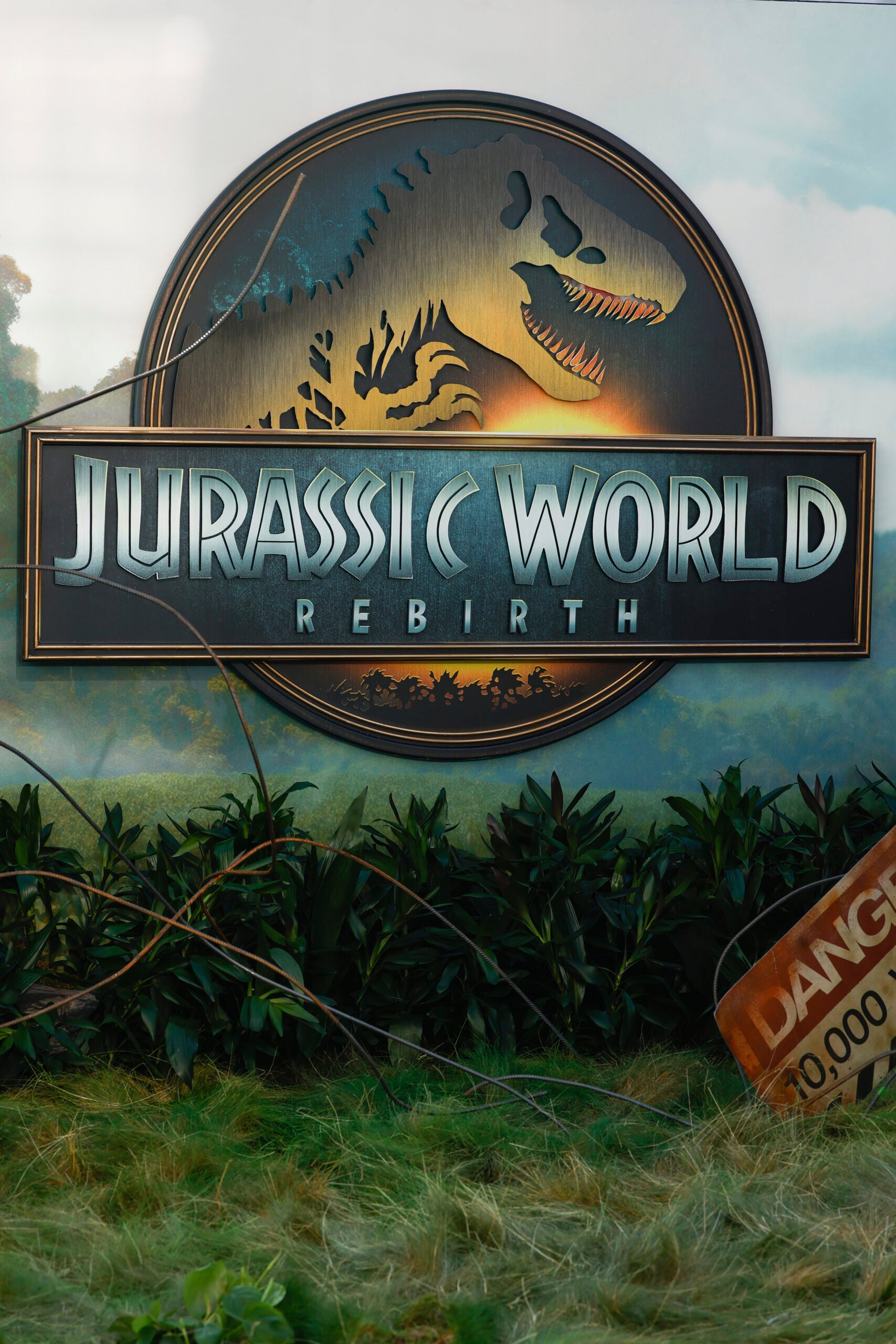 A Jurassic World Rebirth sign is displayed above greenery and grass, with a partially visible Danger warning sign in the lower right corner.