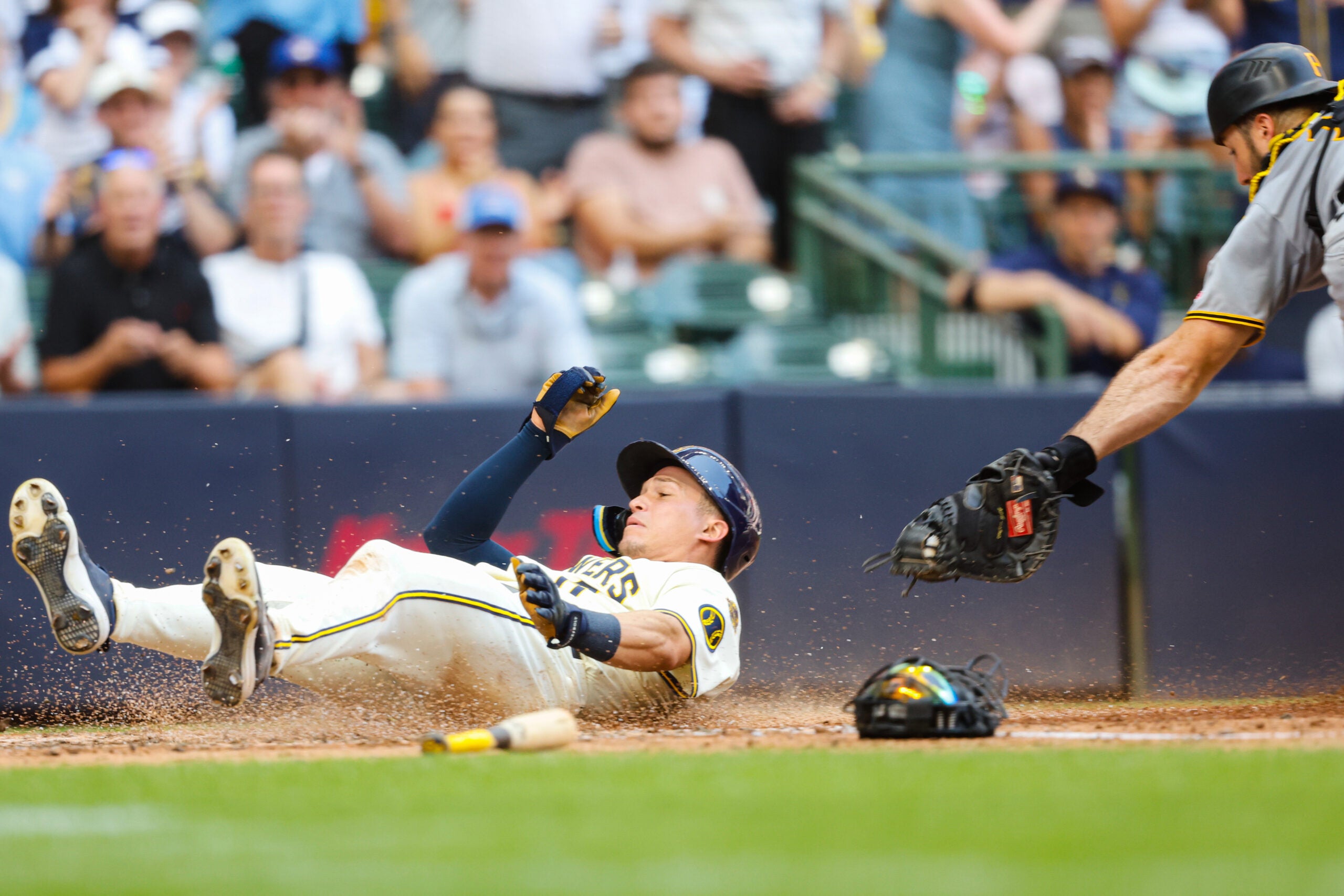 A baseball player slides into home plate as a catcher reaches to tag him during a game, with the crowd watching in the background.