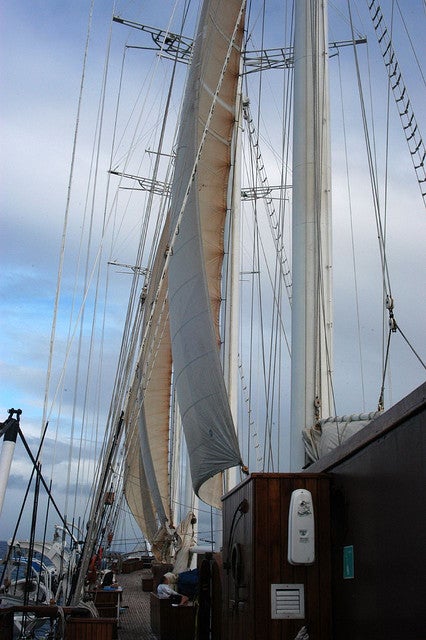Tall sailboat masts and rigging viewed from the deck, with a partly cloudy sky in the background.