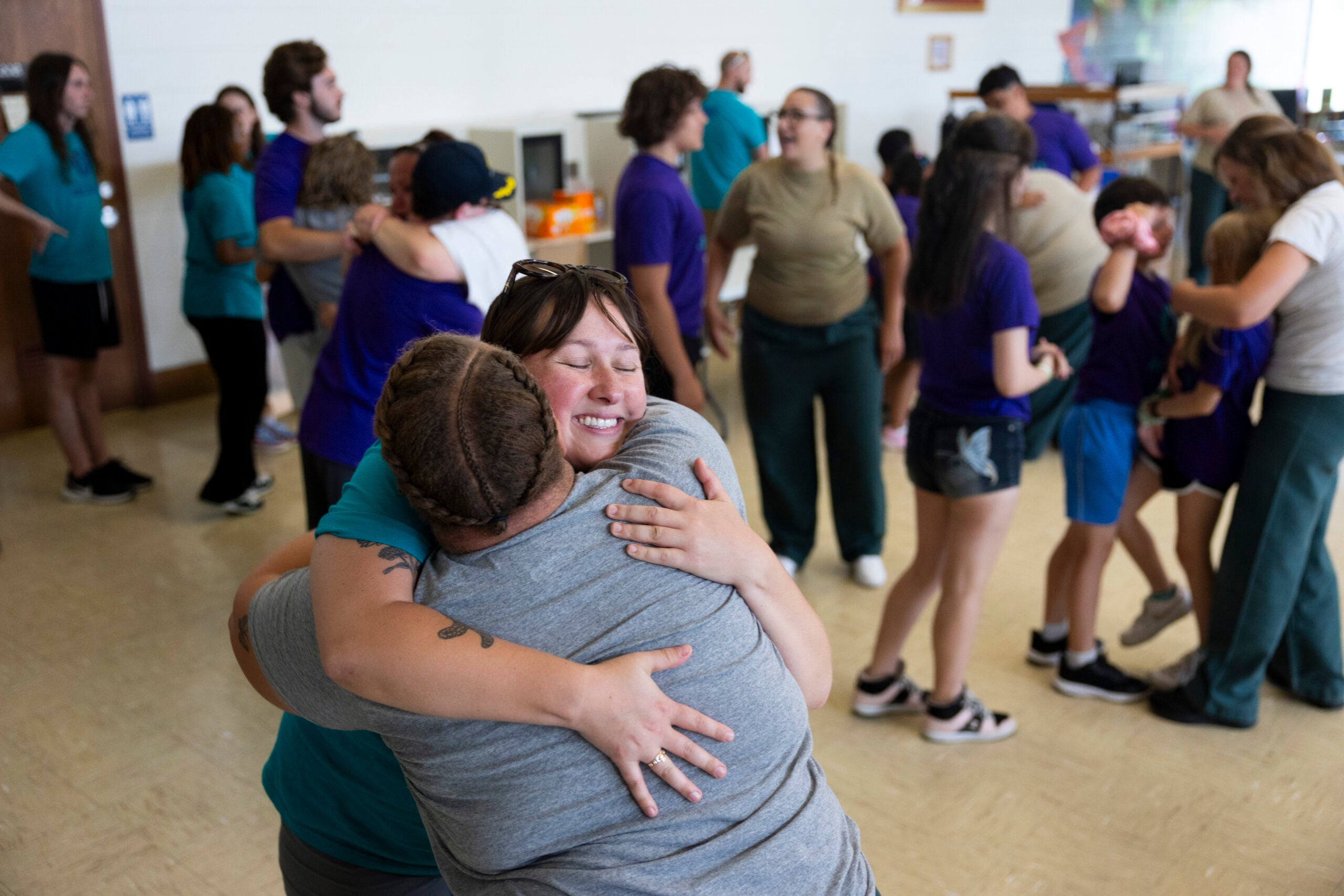 A group of people in a brightly lit room, some hugging and others talking or standing in small groups, creating a lively and social atmosphere.
