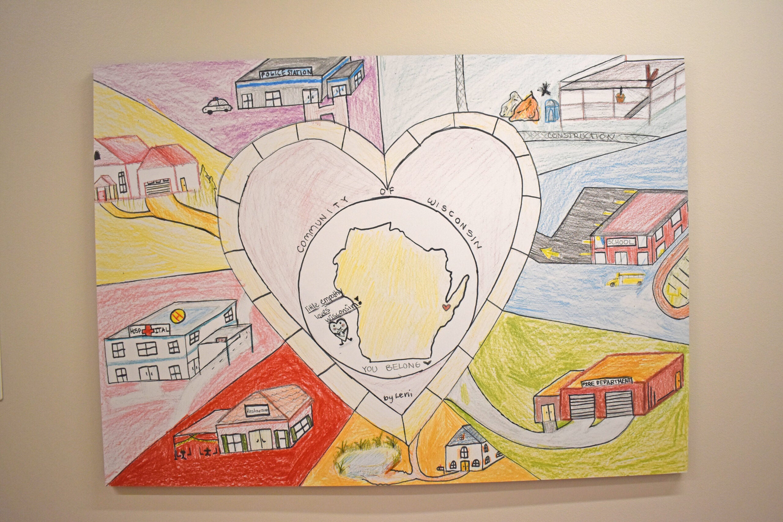 A hand-drawn map of Wisconsin inside a heart, surrounded by colorful sketches of community buildings and roads, with the text “Community of Wisconsin” and “You Belong.”.