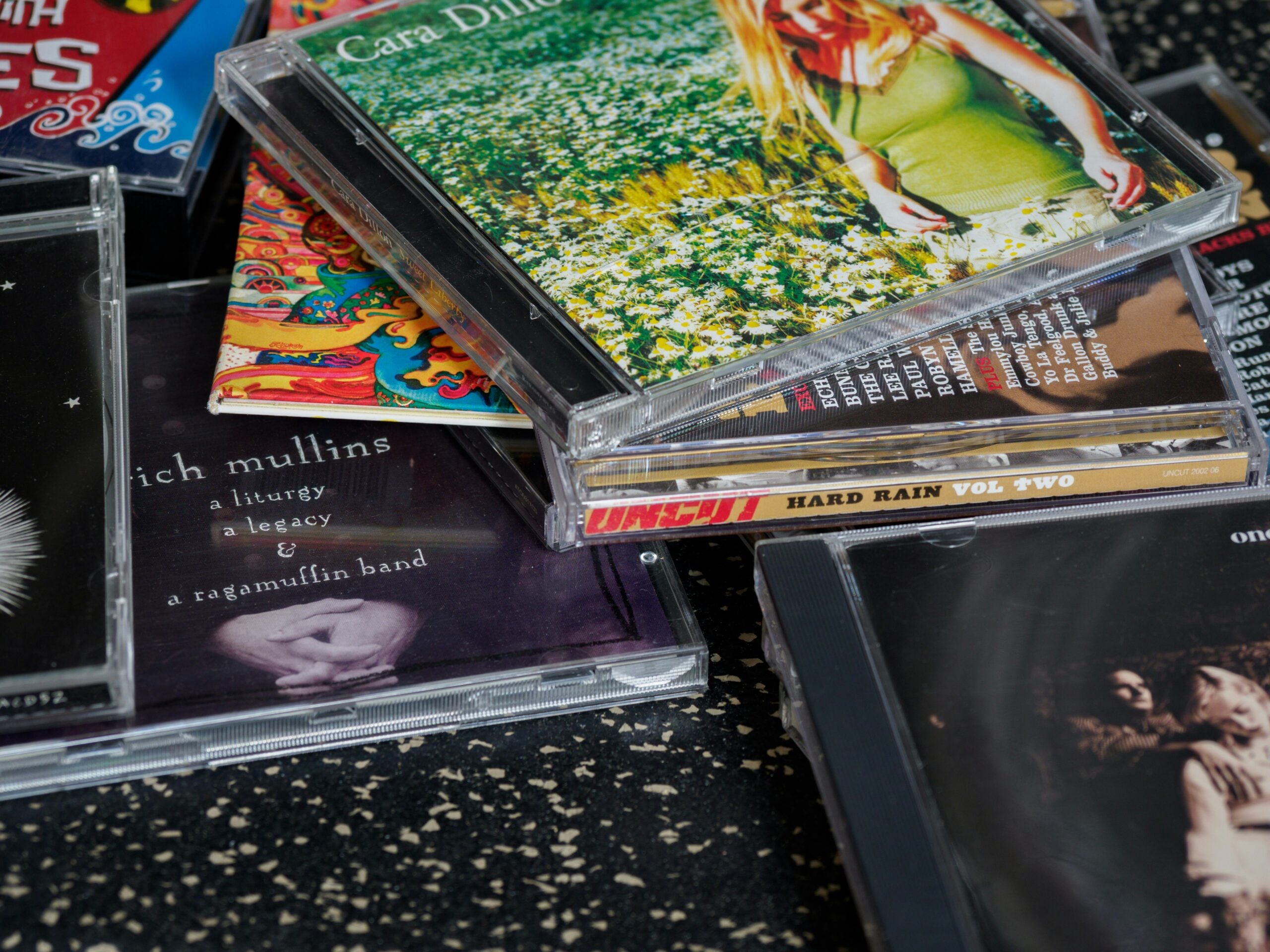 A stack of assorted music CDs, some with visible covers and titles, arranged on a speckled black and white surface.