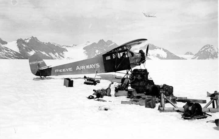 A single-propeller Reeve Airways plane sits on snowy ground surrounded by machinery parts, with mountains in the background.