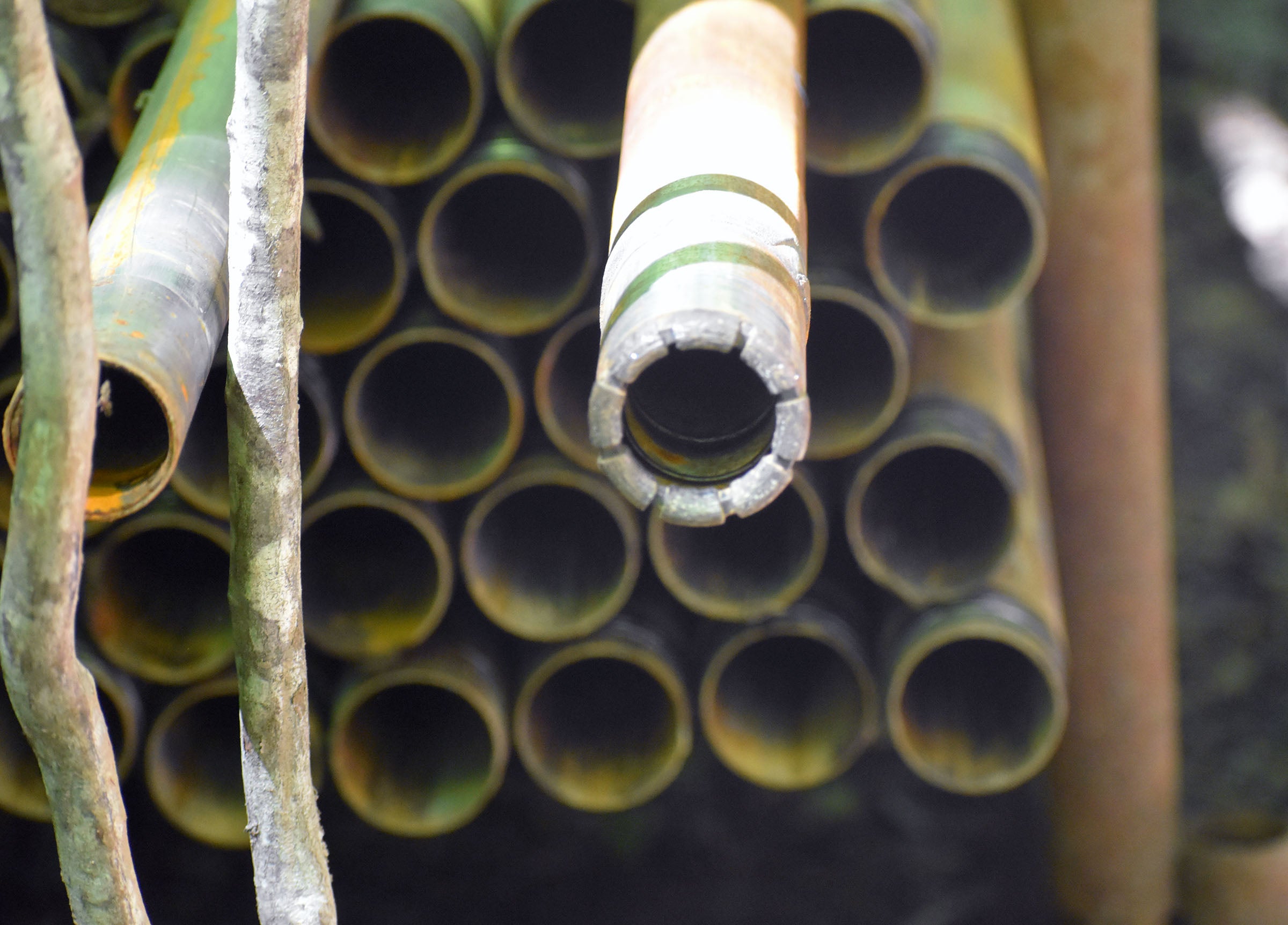 Close-up of stacked metal pipes with one pipe facing forward, showing its inner threading and detail, surrounded by other pipes and rods.