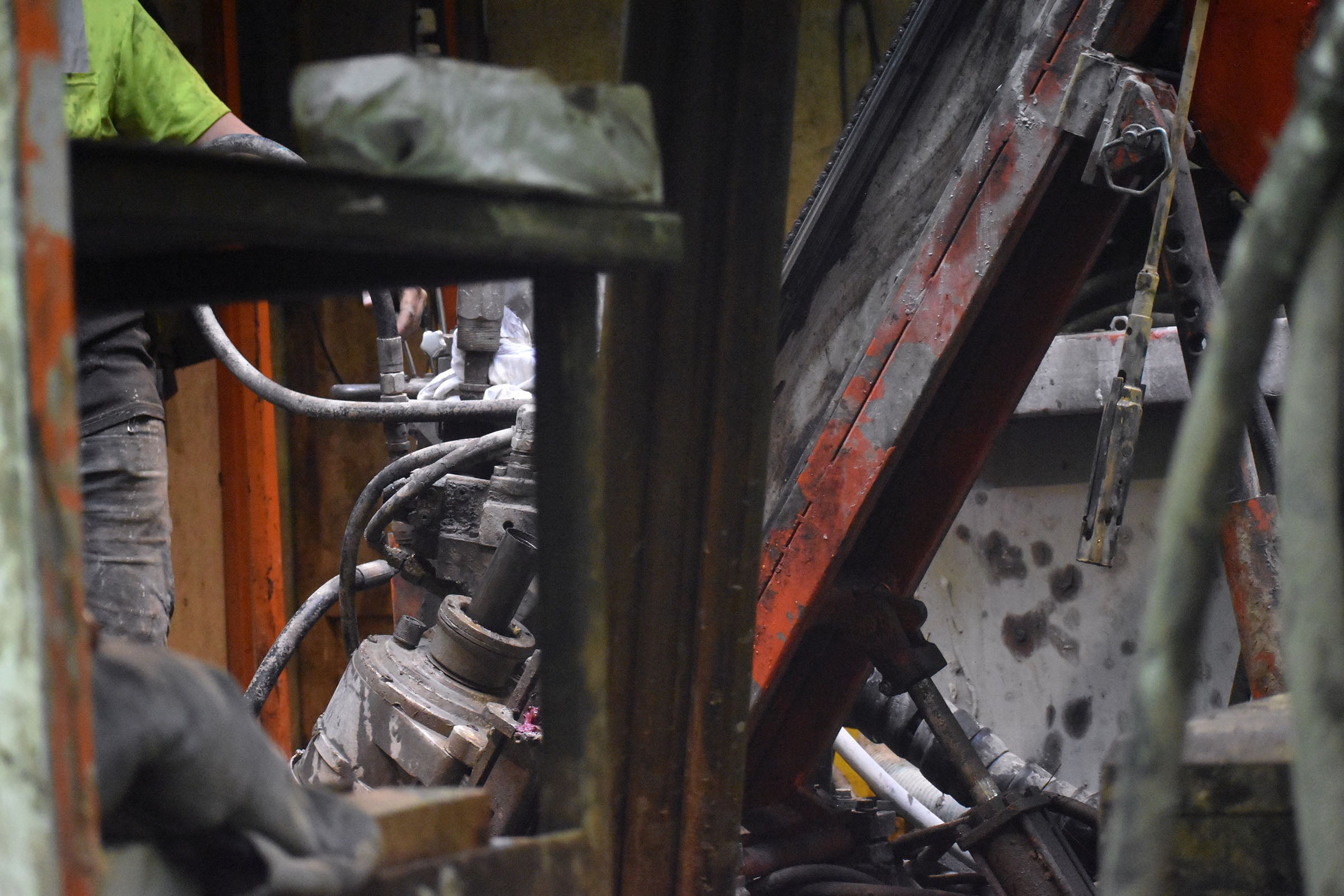 A worker operates heavy machinery with hydraulic hoses and metal components in an industrial setting.