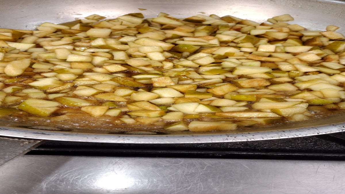 Chopped apples cooking in a skillet with liquid, likely being prepared for a recipe on a stovetop.