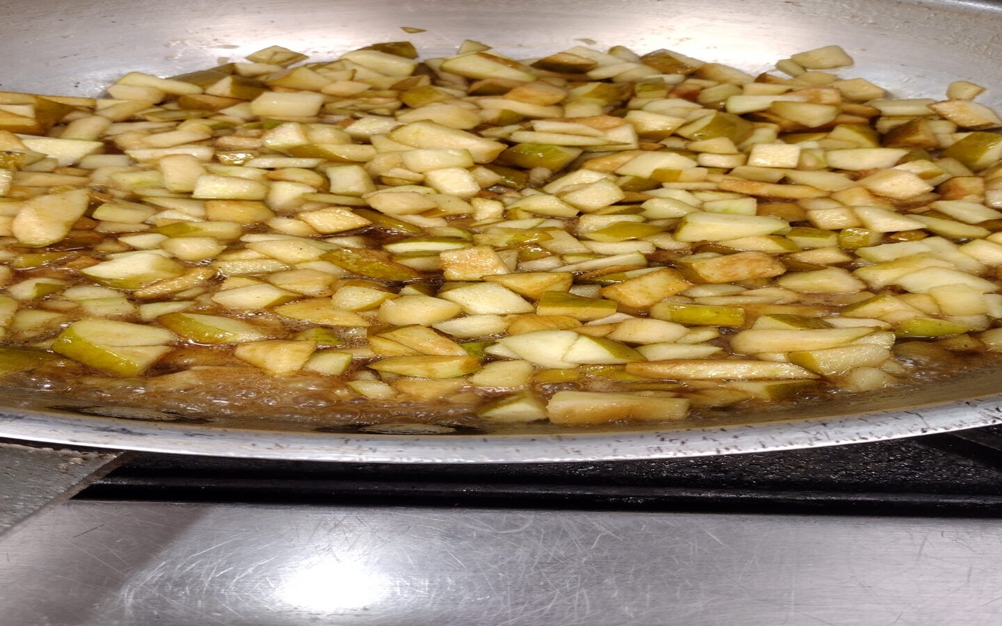 Chopped apples cooking in a skillet with liquid, likely being prepared for a recipe on a stovetop.