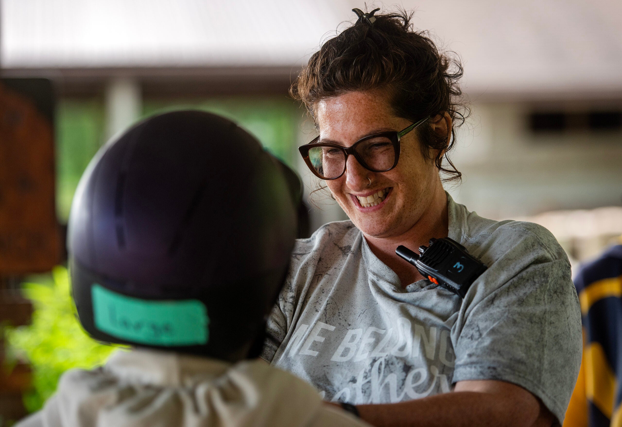 A woman with glasses and a microphone smiles while interacting with a person wearing a helmet and a shirt labeled Lucas.