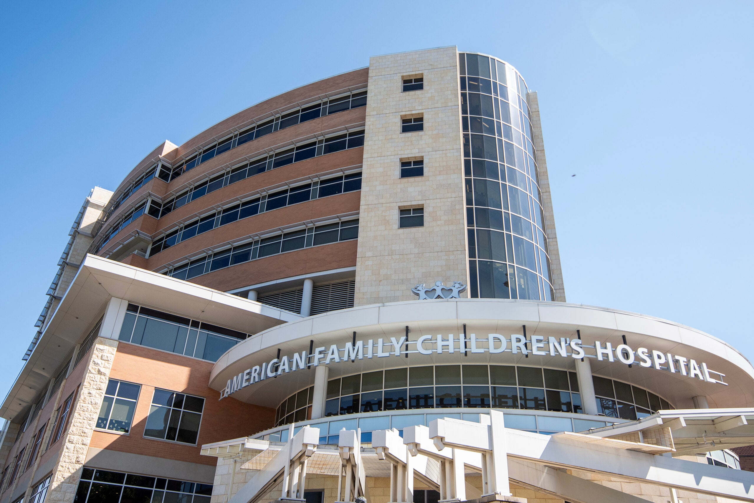 A modern multi-story building with glass and stone features, displaying the sign American Family Childrens Hospital under a clear blue sky.