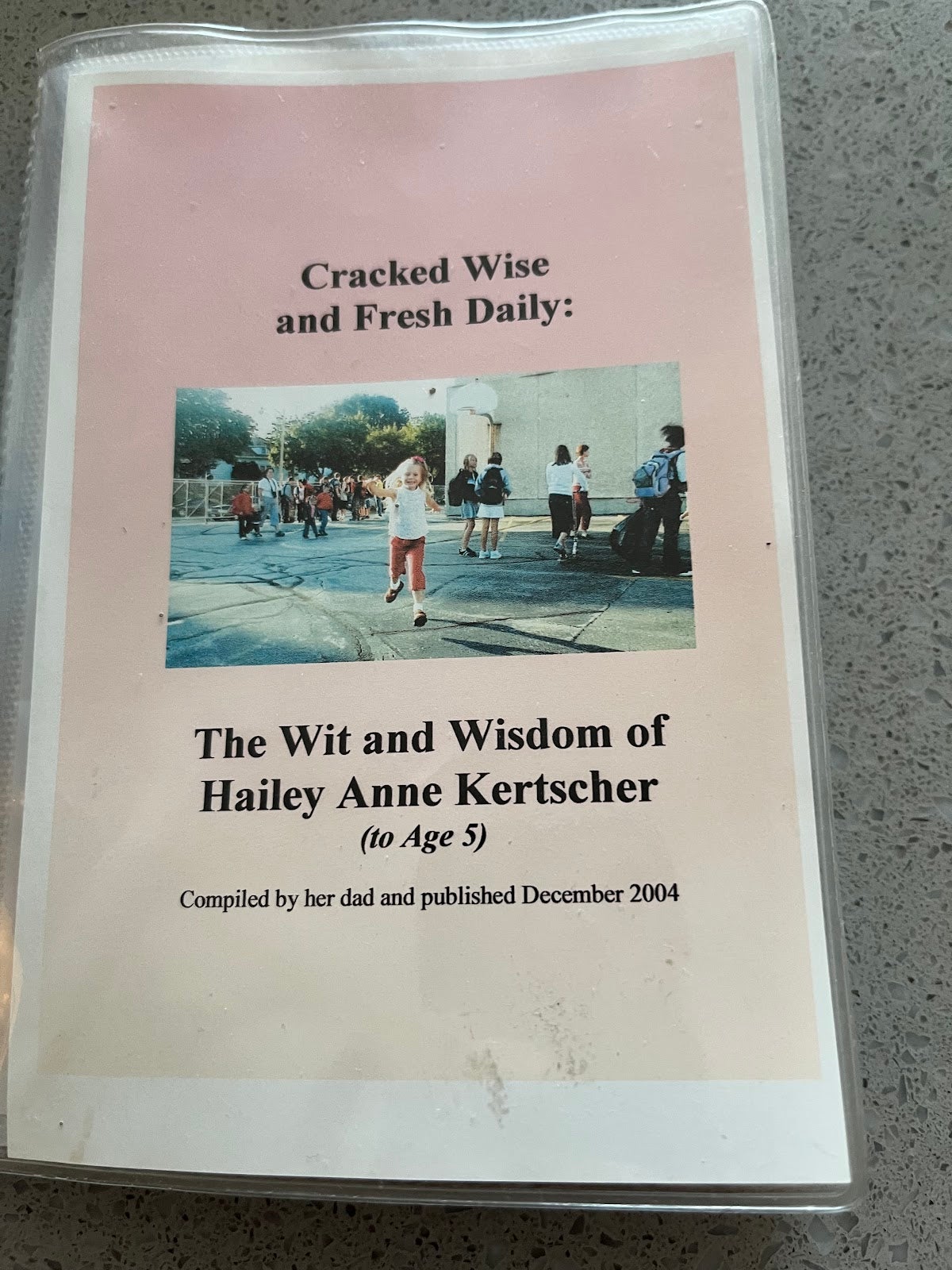 A booklet cover titled The Wit and Wisdom of Hailey Anne Kertscher (to Age 5), featuring a photo of children outside, compiled by her dad and published December 2004.