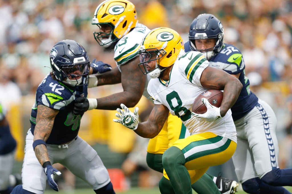A Green Bay Packers player runs with the football while being pursued by Seattle Seahawks defenders during a game.